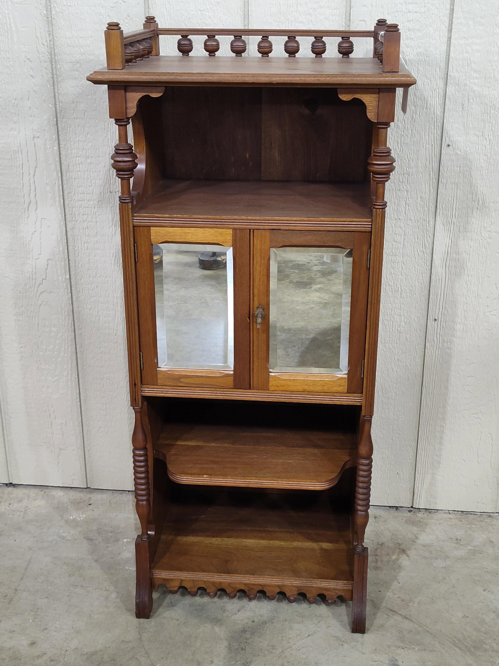 Beautiful Walnut Music Cabinet: Early 20th C walnut cabinet with 3 open shelves and one enclosed shelf with beveled mirrored doors. The top features stick and ball spindle style decorations with beveled wood. Nice clean condition! 1