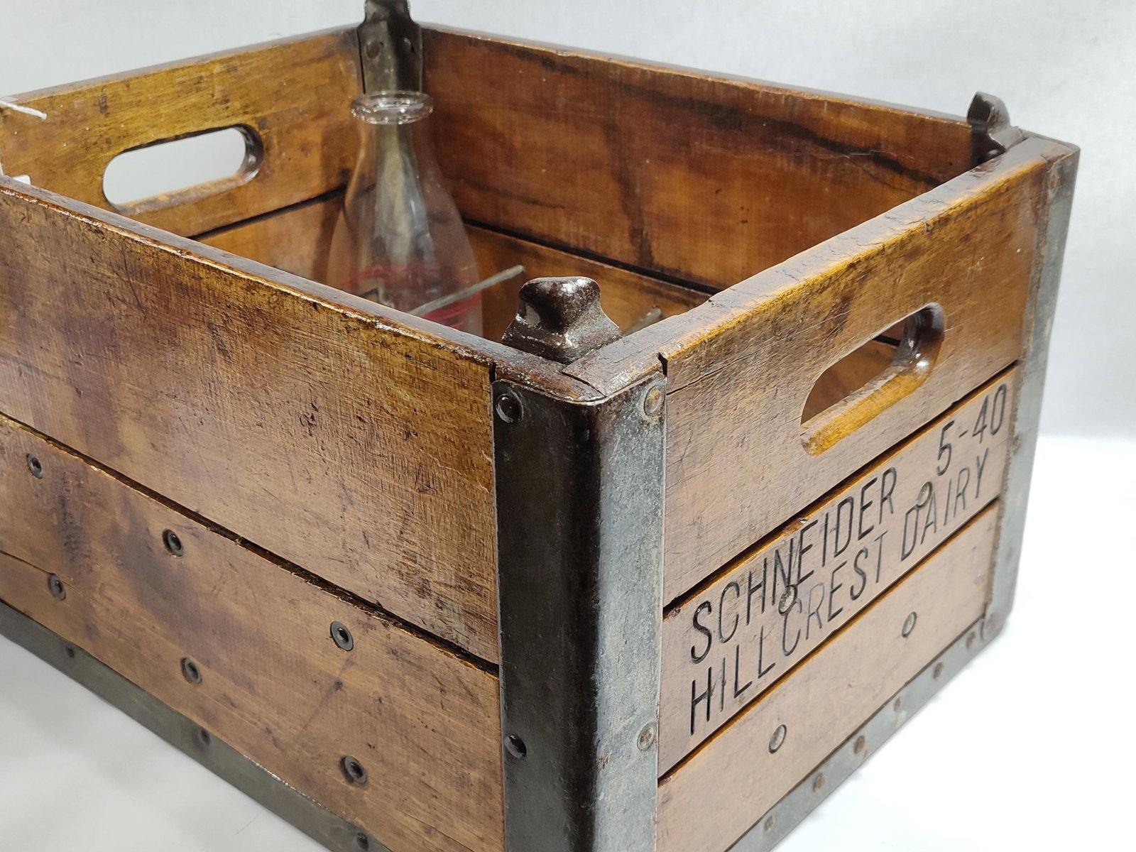 A Pair of Schneider's Hillcrest Dairy Collectibles Including a Wooden Crate and Glass Bottle: This lot features a matchingwooden milk crate and a one-quart glass milk bottle from Schneider's Hillcrest Dairy. The 12-slot crate is constructed from wood panels with galvanized metal reinforcements