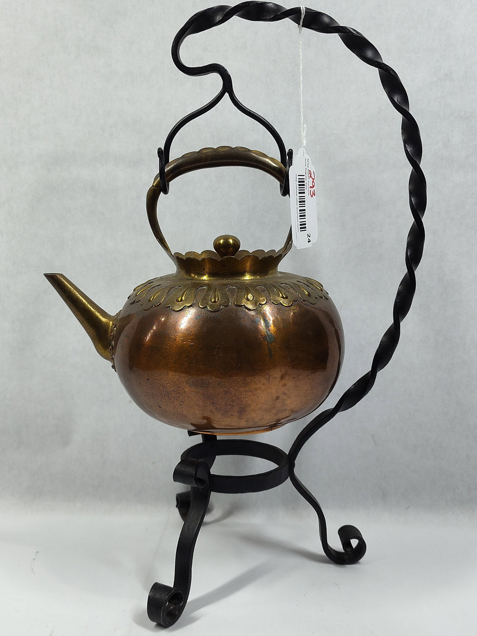 Arts and Crafts Style Copper and Brass Tilting Tea Kettle on Wrought Iron Stand: A decorative tilting spirit kettle presented on a custom wrought iron stand. The kettle features a globular hammered copper body with a contrasting brass collar decorated with a stamped scalloped and 