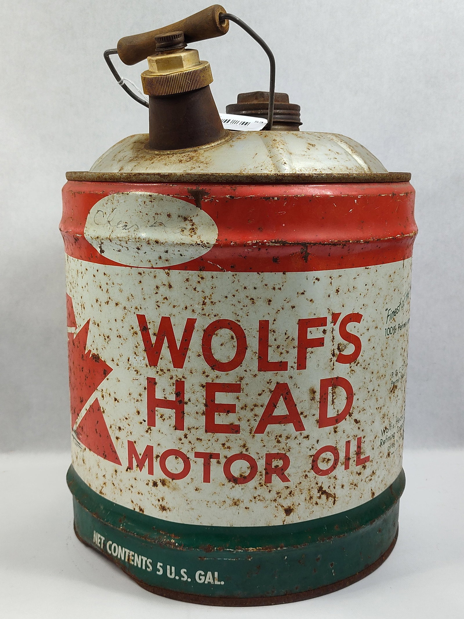 Wolf's Head Motor Oil 5-Gallon Can: Afive-gallon motor oil pail for the Wolf's Head Motor Oil brand. The container is constructed of lithographed metal and features a white body with a red top band and a dark green base band. The front