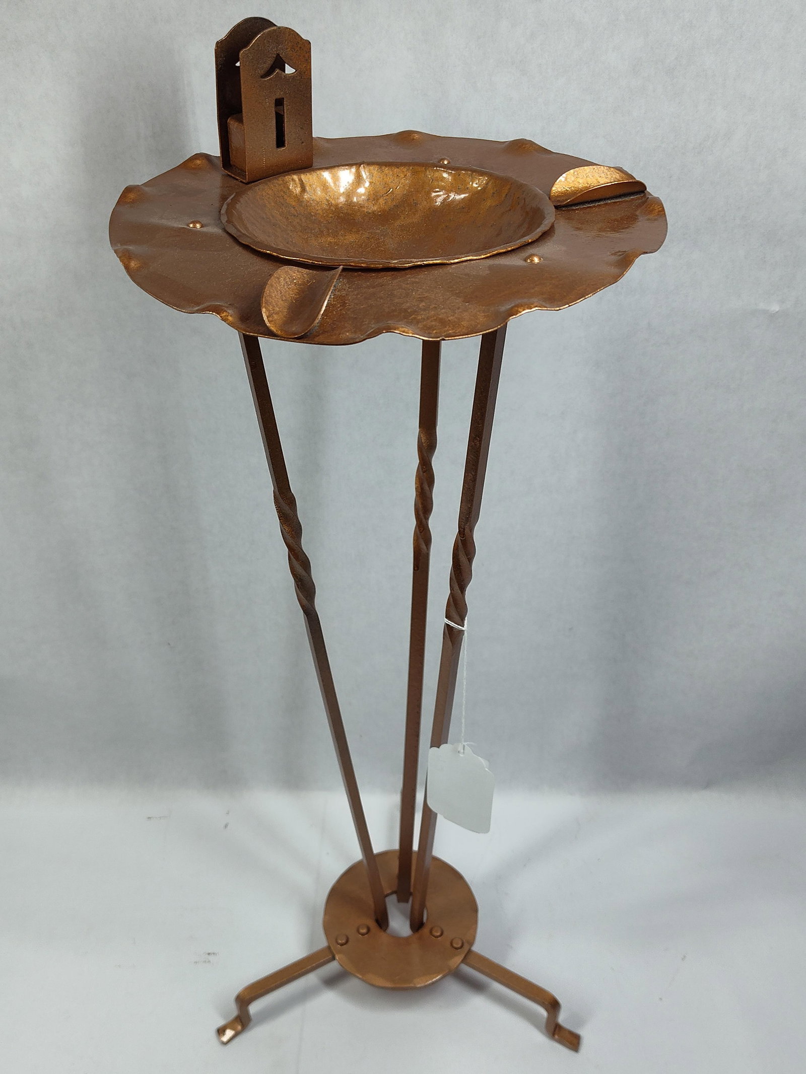 Arts and Crafts Hammered Copper Finished Metal Floor Standing Ashtray: This Arts and Crafts style floor-standing ashtray or smoking stand is constructed from hammered metal with a warm copper-colored finish. The piece features a wide, circular top plate with a