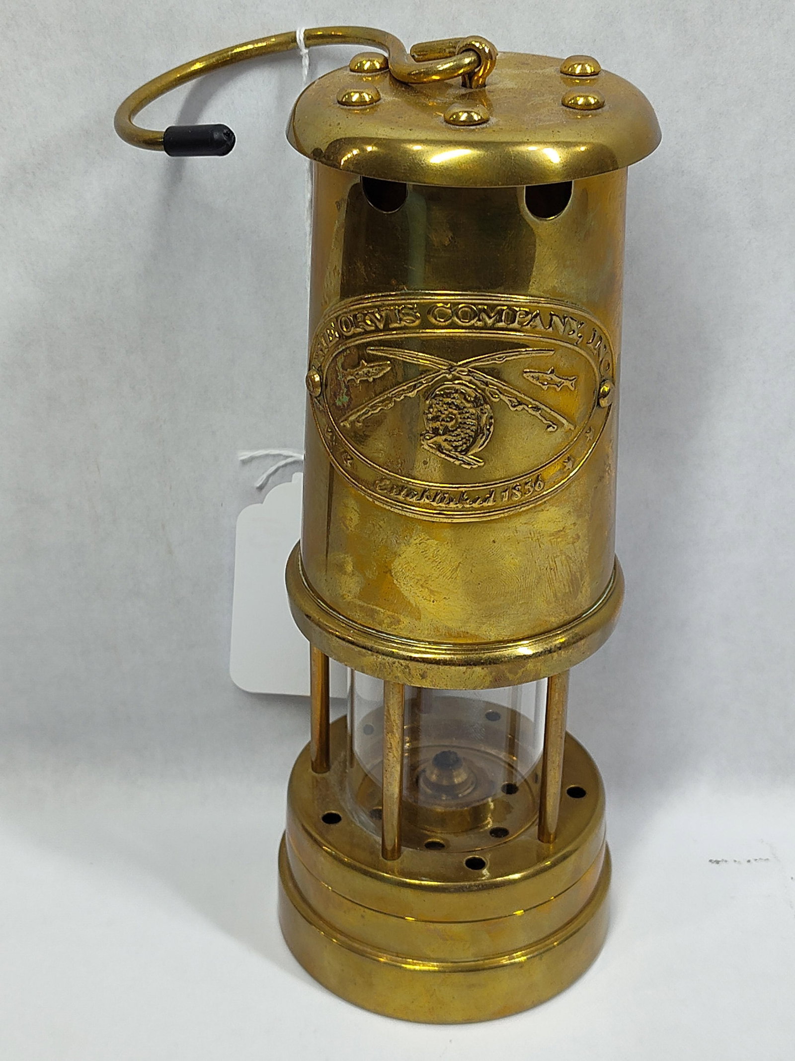 The Orvis Company Inc. Brass Miners Style Safety Lamp: This decorative safety lamp is modeled after a traditional miners oil lantern and is branded for The Orvis Company, Inc. The main cylindrical body features an applied oval brass plaque embossed with