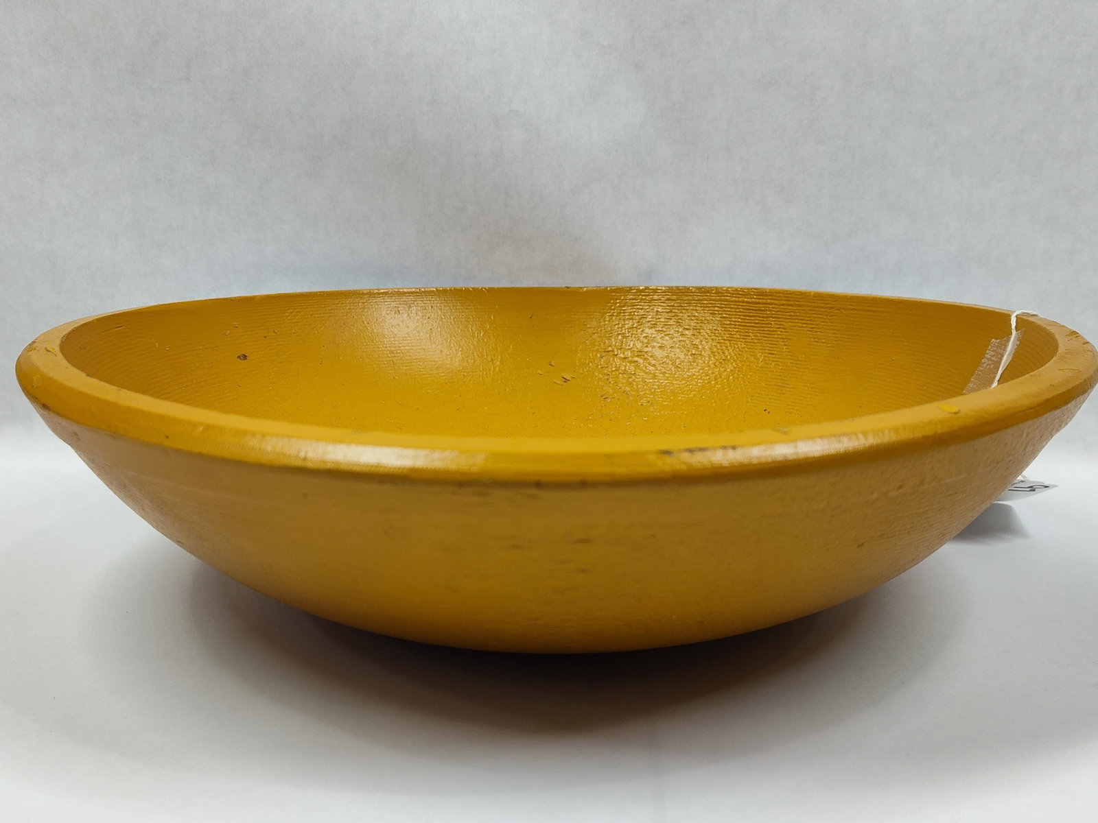 Large Painted Turned Wood Bowl in Mustard Yellow: A large, turned wooden bowl featuring a shallow, round form with wide, tapered sides and a rounded rim. The object is finished entirely in a mustard yellow paint with a slightly glossy surface. The