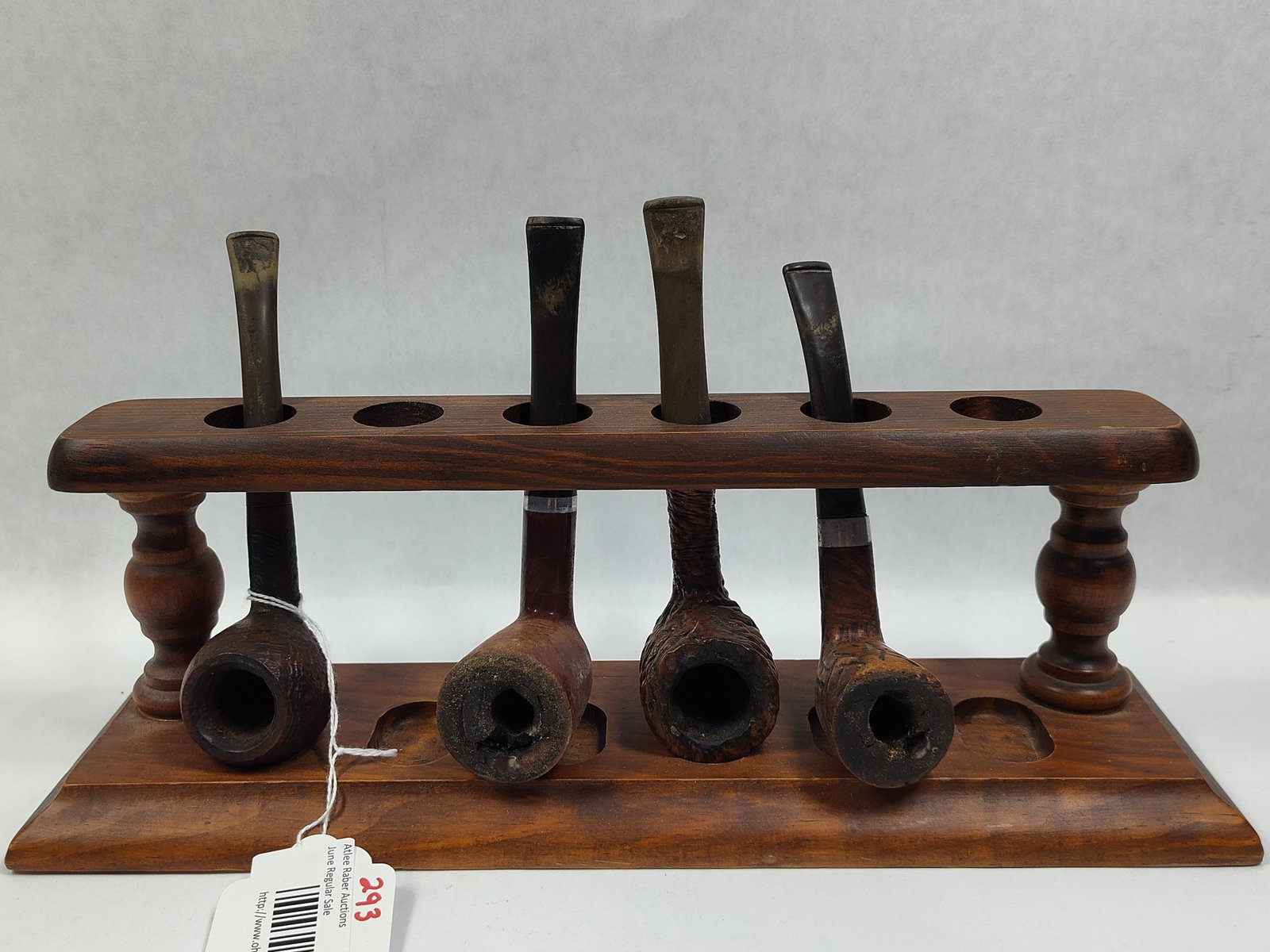 An Assortment of Briar Tobacco Smoking Pipes and a Two-Tier Wooden Rack: An assortment of four tobacco smoking pipes accompanied by a two-tier wooden display rack. The pipes are constructed of briar wood with mouthpieces likely made of vulcanite or ebonite. The collection