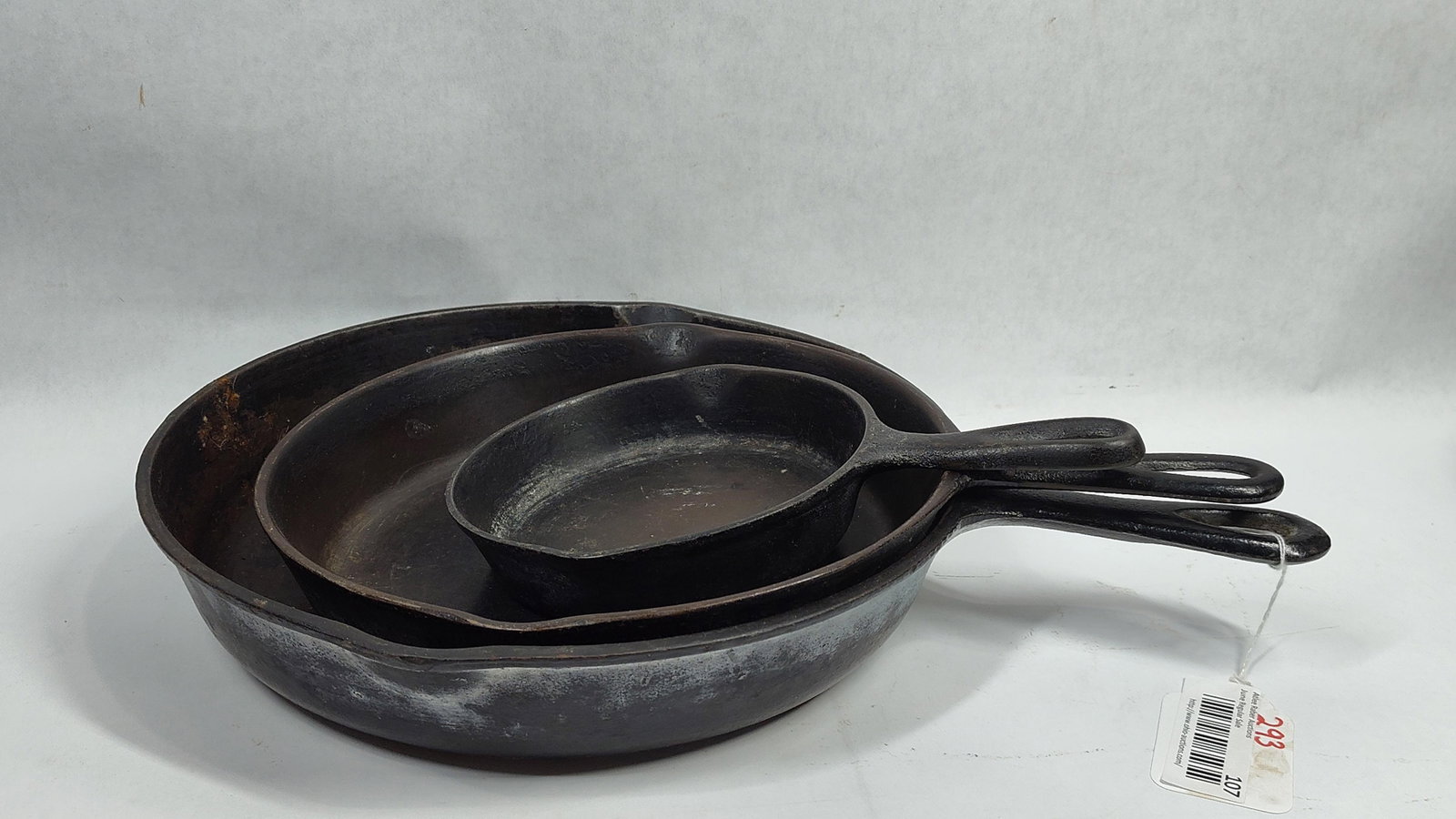 A Trio ofCast Iron Skillets with Notched Heat Rings: A set of three nesting cast iron frying pans of graduated sizes. These skillets feature teardrop-shaped hanging holes and integrated dual pour spouts. The bases are designed with inset heat rings. Eac