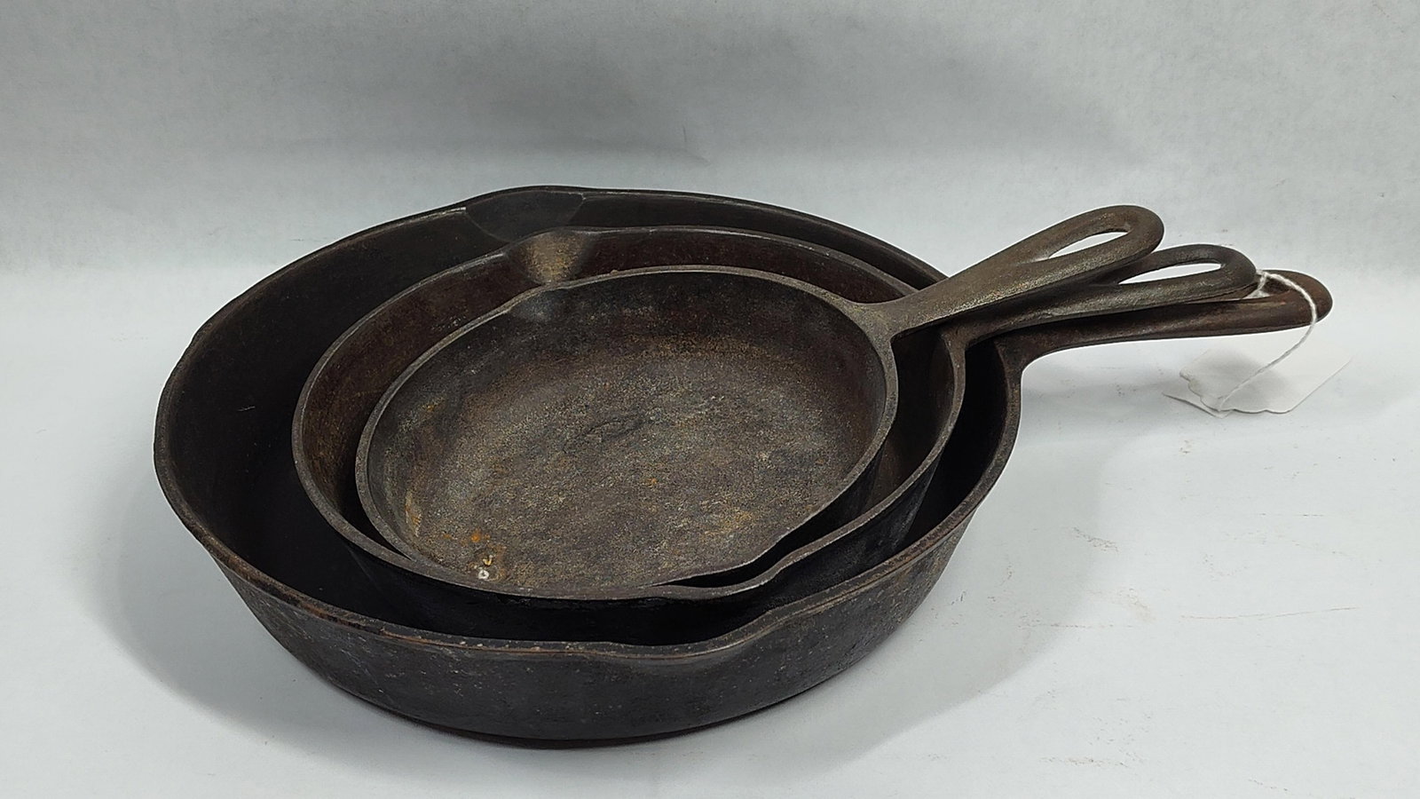 A Trio ofWagner Ware and Lodge Cast Iron Skillets: three graduatedcast iron skillets. The largest skillet is a Wagner Ware example, featuring a smooth base stamped with the maker mark Wagner Ware Sidney -O-. The handle is incised with the number 8