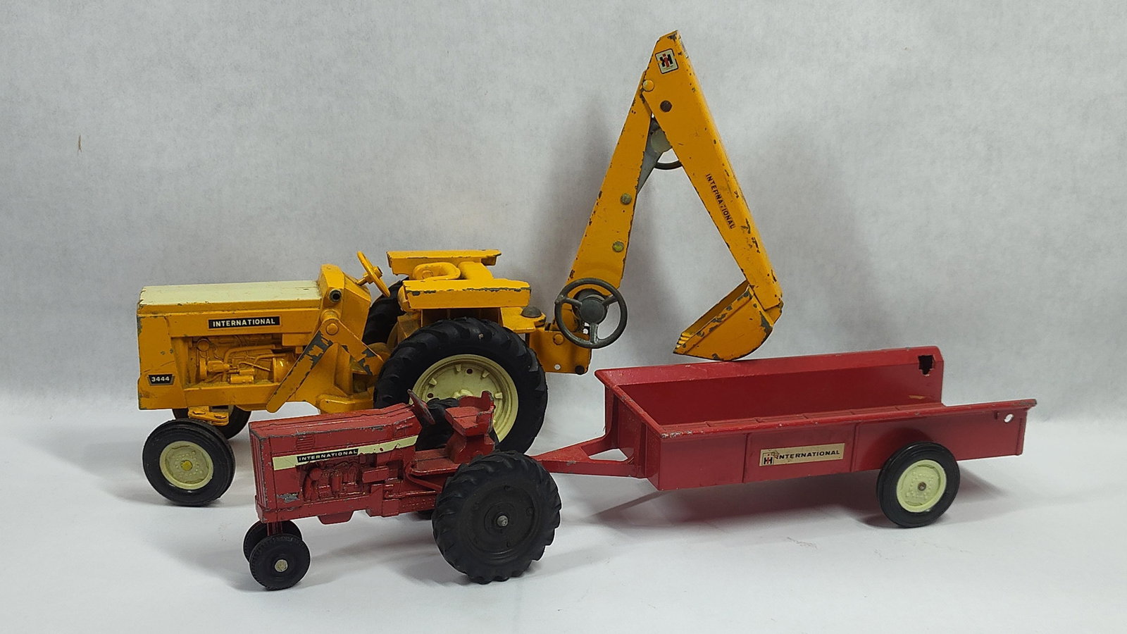 Three Ertl International Harvester Die-Cast Metal Toys: This lot comprises three die-cast metal toys manufactured by the Ertl Company, modeled after International Harvester equipment. The first item is an International 3444 industrial backhoe loader finish