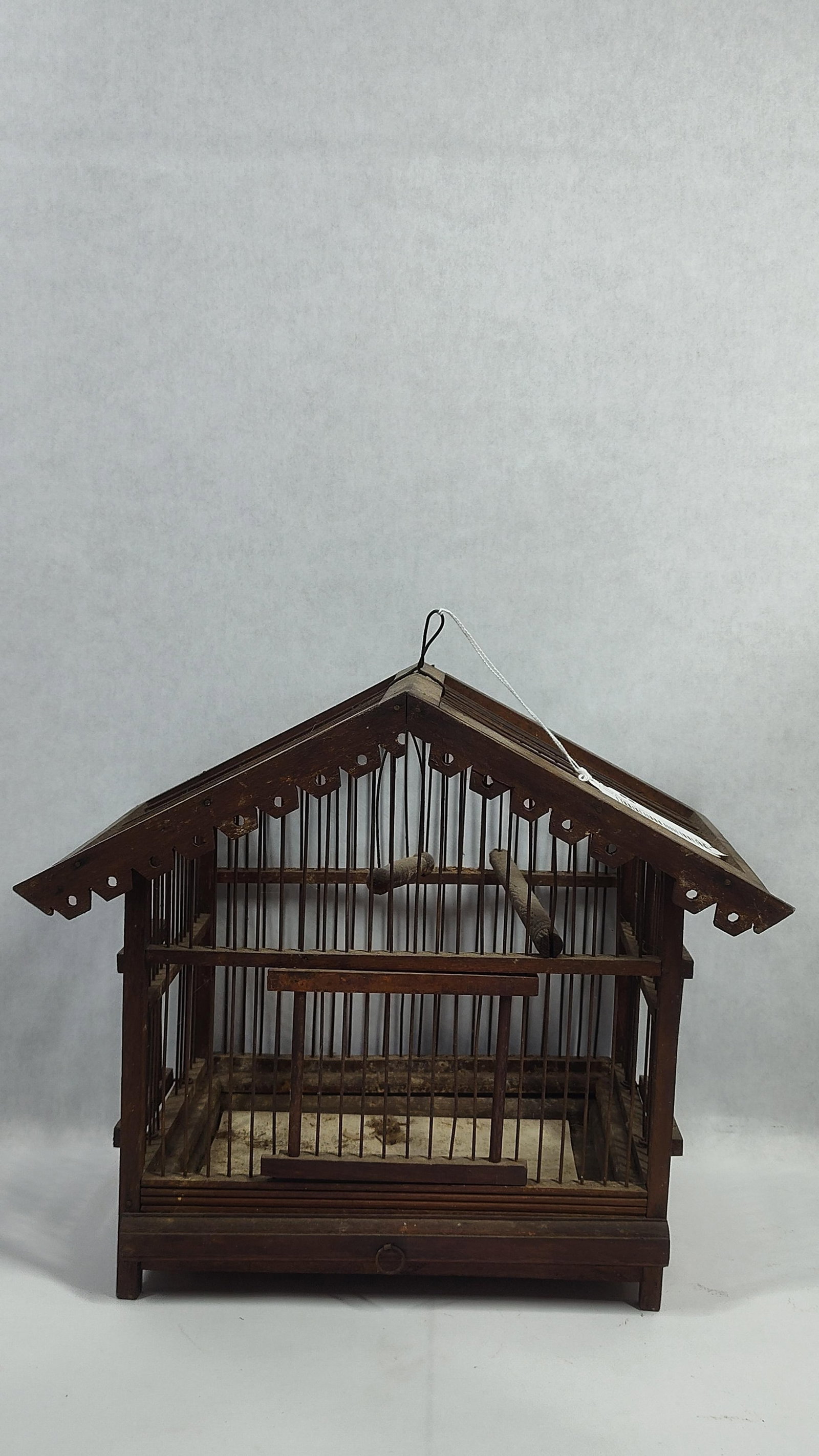 Victorian Style Wooden and Wire House-Form Birdcage: An antique house-form birdcage constructed from dark-stained wood and vertical metal wires. The structure features a gabled roof with decorative scalloped and pierced detailing along the eaves. The ca