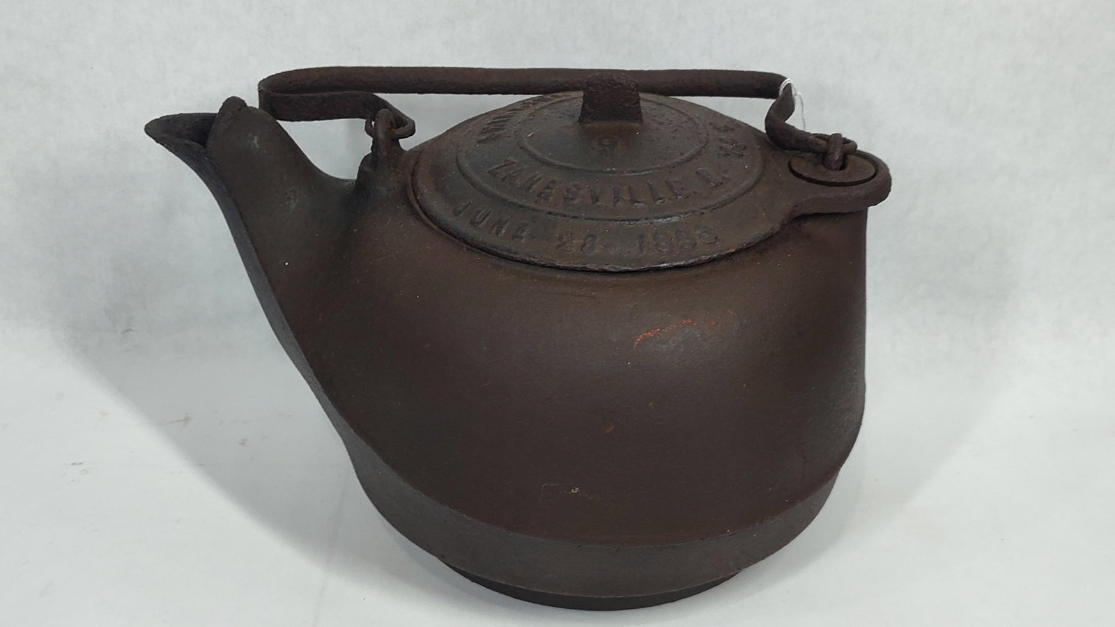 American Shantz Zanesville Cast Iron Swivel Lid Tea Kettle Dated 1853: This mid-19th-century American tea or hearth kettle is constructed from heavy cast iron and was produced in Zanesville, Ohio. The vessel features a wide, rounded body with an integrated spout and a fl