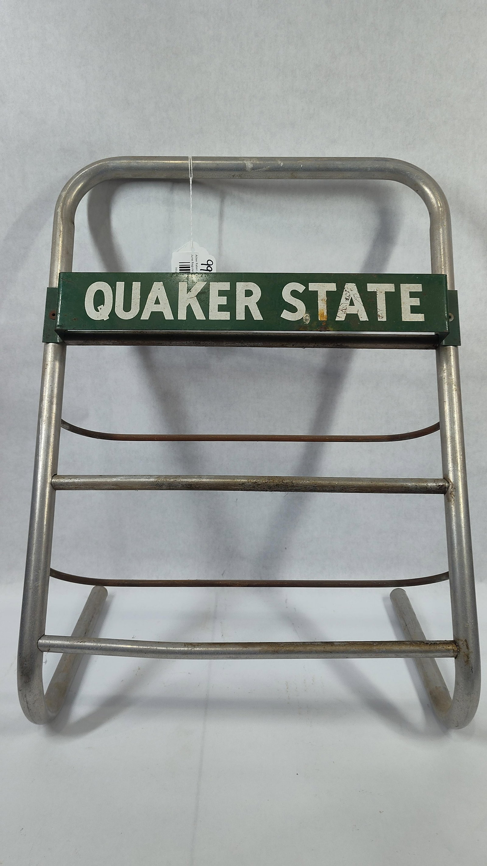 Quaker State Three-Tier Tubular Metal Oil Can Display Rack: AQuaker State motor oil promotional display rack featuring a tubular metal frame. The structure consists of a silver-toned metal tube forming a curved handle at the top and support legs at the base. A