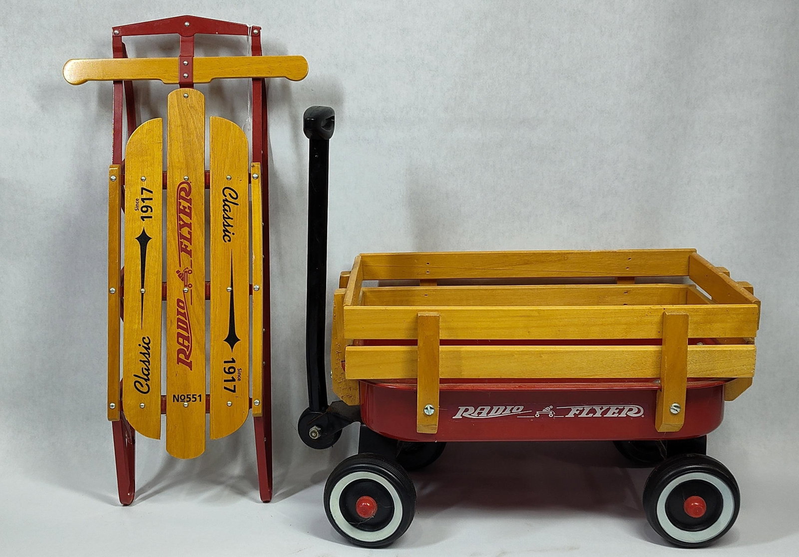 A Pair of Radio Flyer Collectible Toys Including a No. 551 Classic Sled and a Miniature Stake Side: This lot consists of two collectible toys manufactured by Radio Flyer. The first item is a No. 551 Classic model runner sled constructed with three natural-finish wood slats and a wooden steering cros