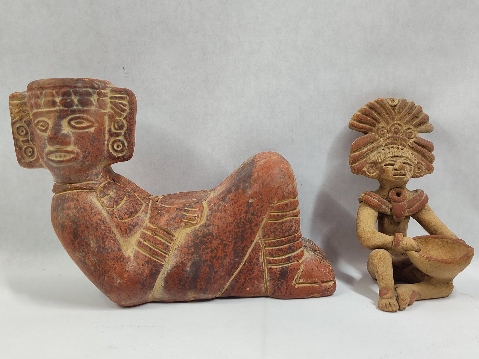 Two Pre-Columbian Style Ceramic Figurines: This lot features two figurative ceramic sculptures rendered in the style of ancient Mesoamerican cultures. The first figure is modeled in the reclining Chacmool form, characteristic of Toltec and May