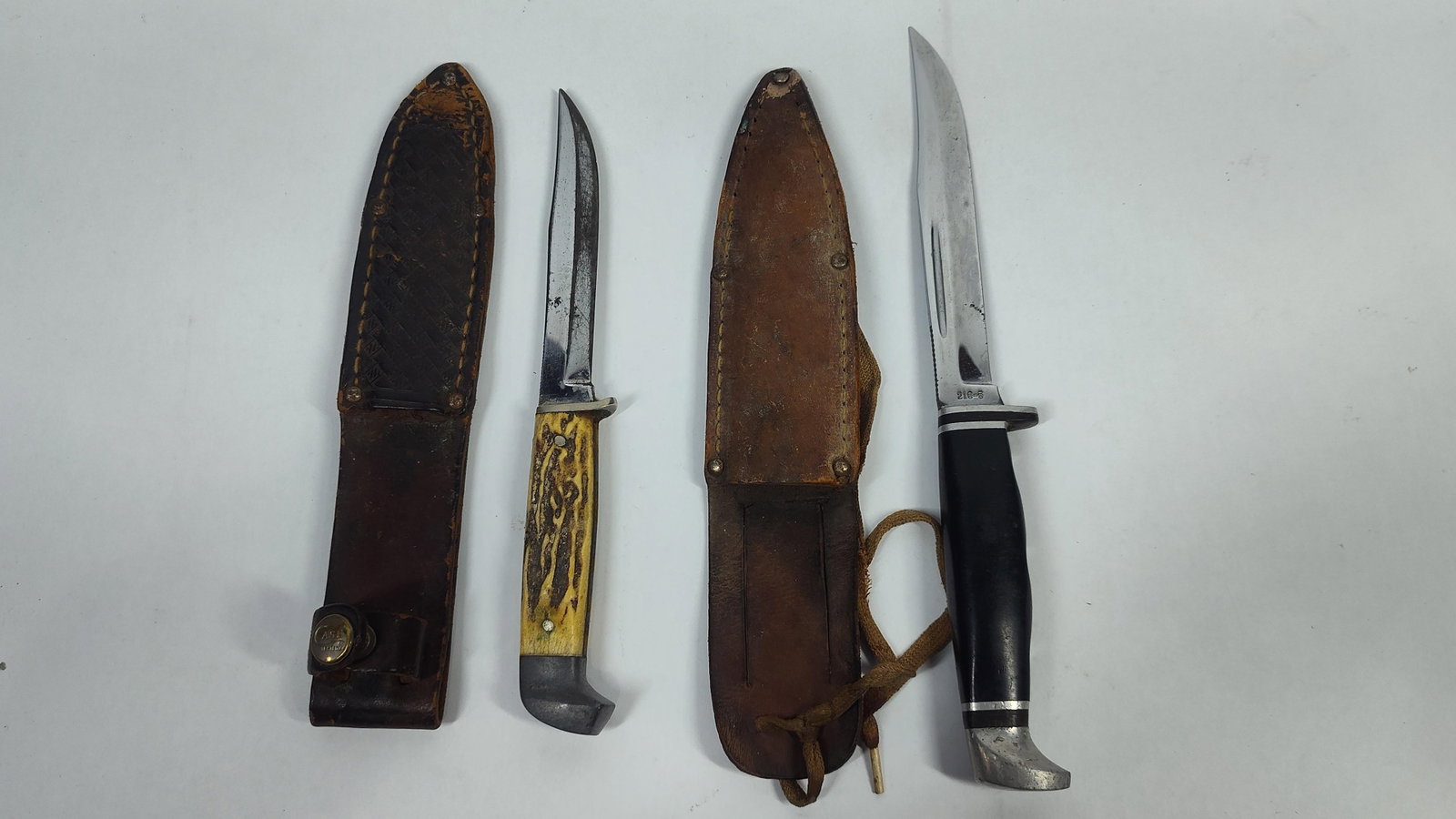 TwoCase Fixed Blade Hunting Knives with Leather Sheaths: This lot features two American-made fixed blade hunting knives manufactured by Case. The first knife is a clip-point hunter with a tang stamp reading CASE. The handle is constructed of jigged bone or