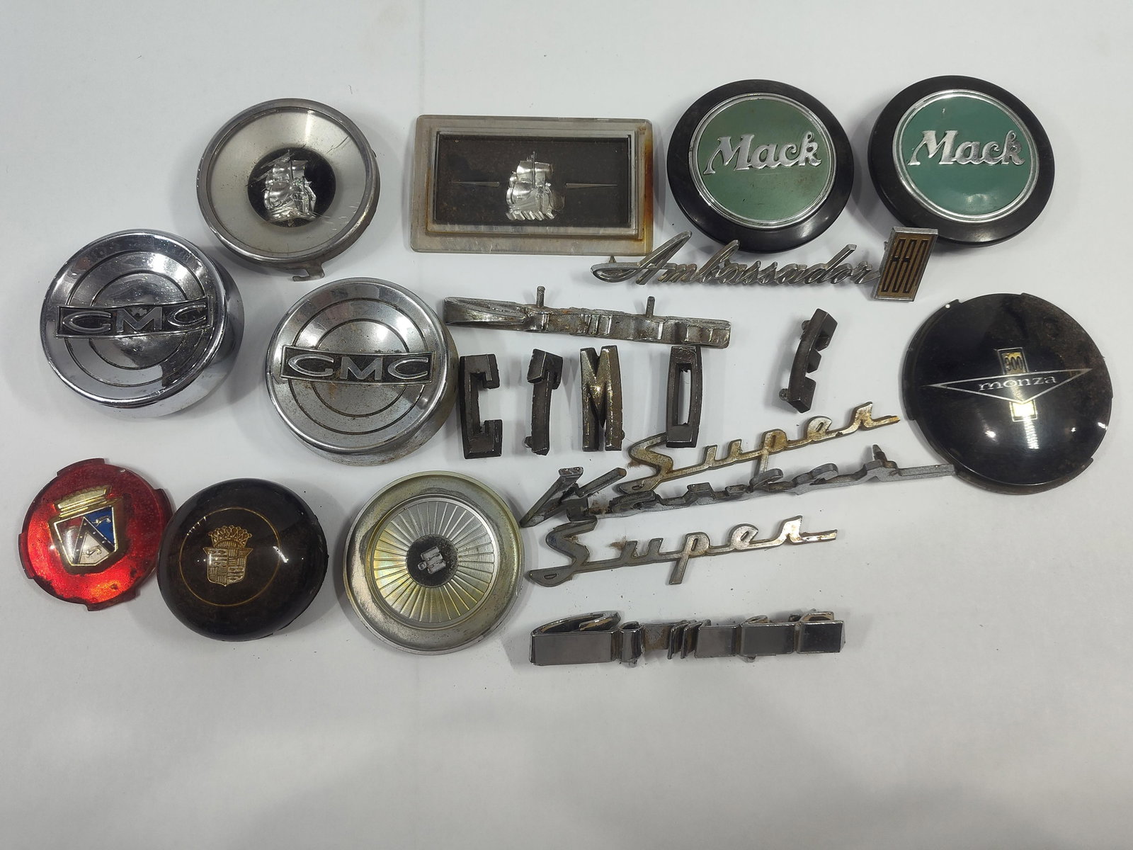 approximately 18Automotive Emblems, Script Badges, and Hubcap Centers: This lot consists of an assortment ofautomotive trim and identification pieces dating approximately from the 1940s through the 1960s. Notable manufacturers represented include Mack Trucks with two