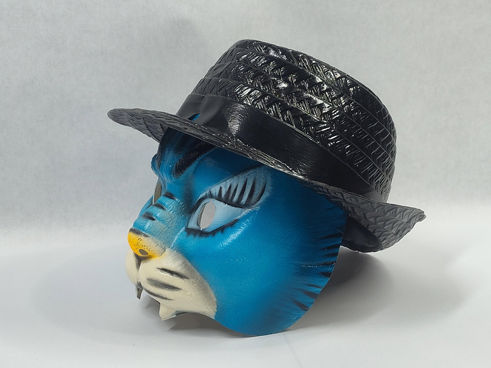 Character Mask in the Style of Top Cat: Acharacter mask depicting an anthropomorphic blue feline wearing a black hat, resembling the cartoon character Top Cat. The item is constructed from thin-gauge vacuum-formed plastic. The facial featur