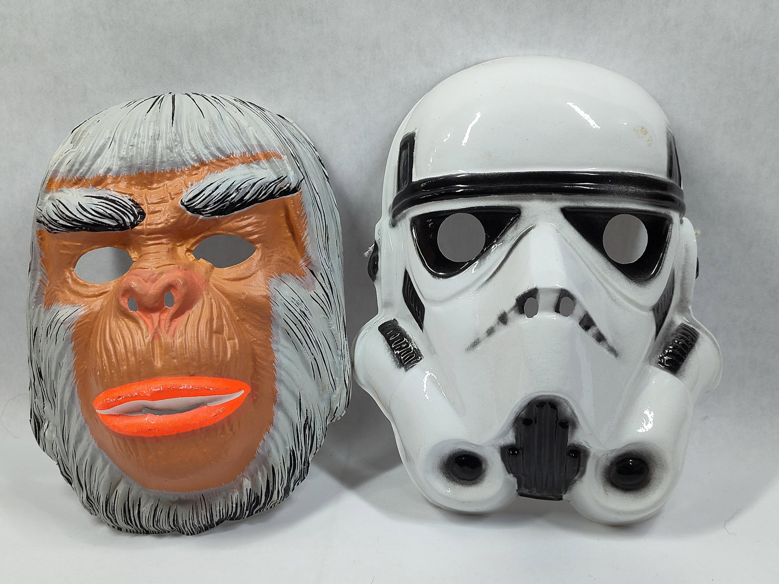 A Pair ofVacuum-Formed Plastic Halloween Masks including Licensed 1977 Star Wars Stormtrooper: This lot consists of a pair ofvacuum-formed thin plastic Halloween masks, dating to the late 1970s. The first mask depicts a stylized primate face with white hair, tan skin, and prominent orange lips,