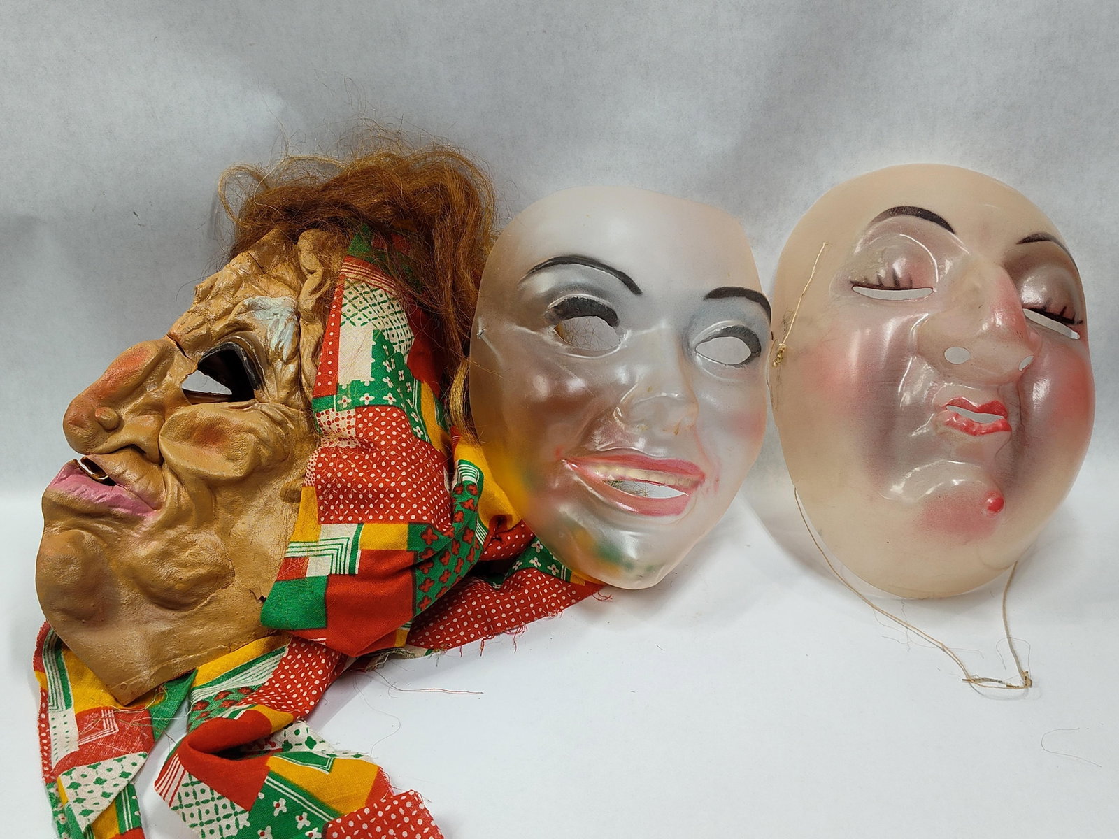 ThreeHalloween Masks Including Molded Latex and Translucent Plastic: threeHalloween masks. The first mask is constructed of molded latex and depicts a crone or witch character. It features deep facial wrinkles, an exaggerated nose, and a single protruding white tooth. 
