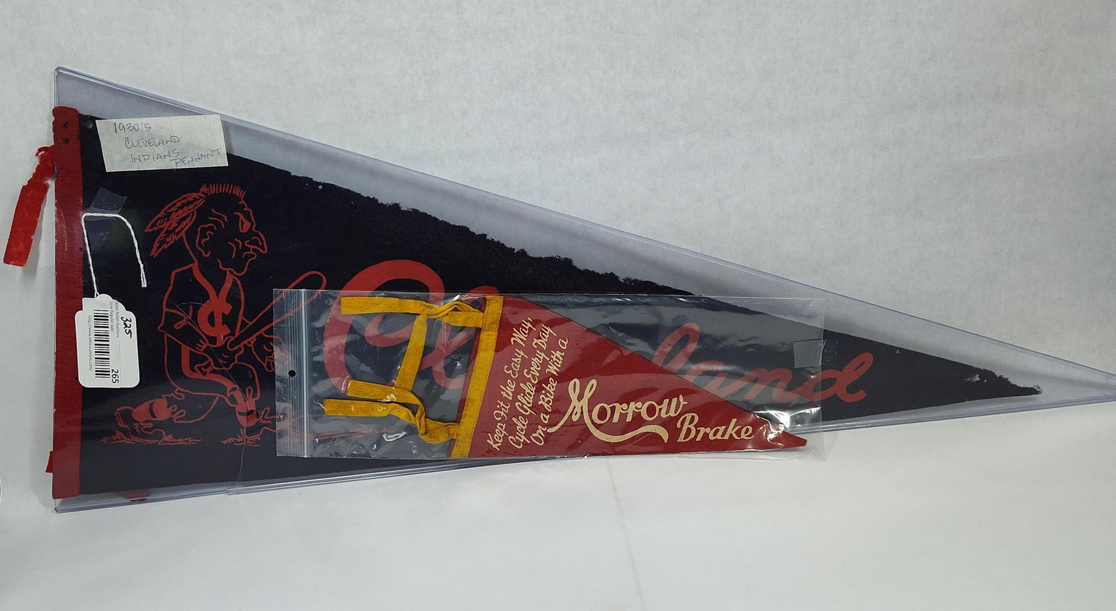 TwoFelt Pennants Including Cleveland Indians and Morrow Brake Advertising: twofelt pennants. The larger pennant is a Cleveland Indians baseball souvenir constructed of dark felt with red printed graphics. The design features a caricature mascot in a batting stance and the ci