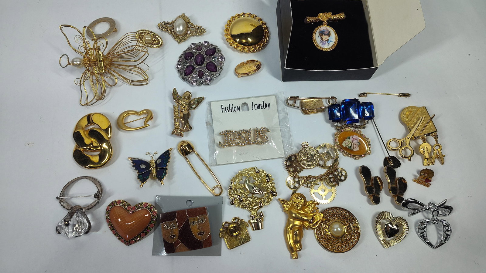 26 Costume Jewelry Brooches and Pins: This collection consists of 26 costume jewelry brooches and pins featuring an assortment of figural, religious, and abstract motifs. The pieces are constructed from gold-tone and silver-tone base meta