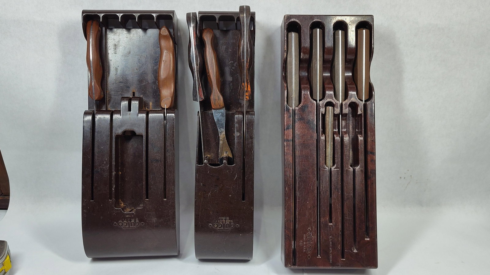 A Set of TenCutco Cutlery Pieces and Three Wall-Mount Storage Blocks: A set of tenCutco cutlery pieces and three coordinating wall-mount storage blocks. The tools are constructed with high-carbon stainless steel blades and marbled dark brown thermo-resin handles. Stampe
