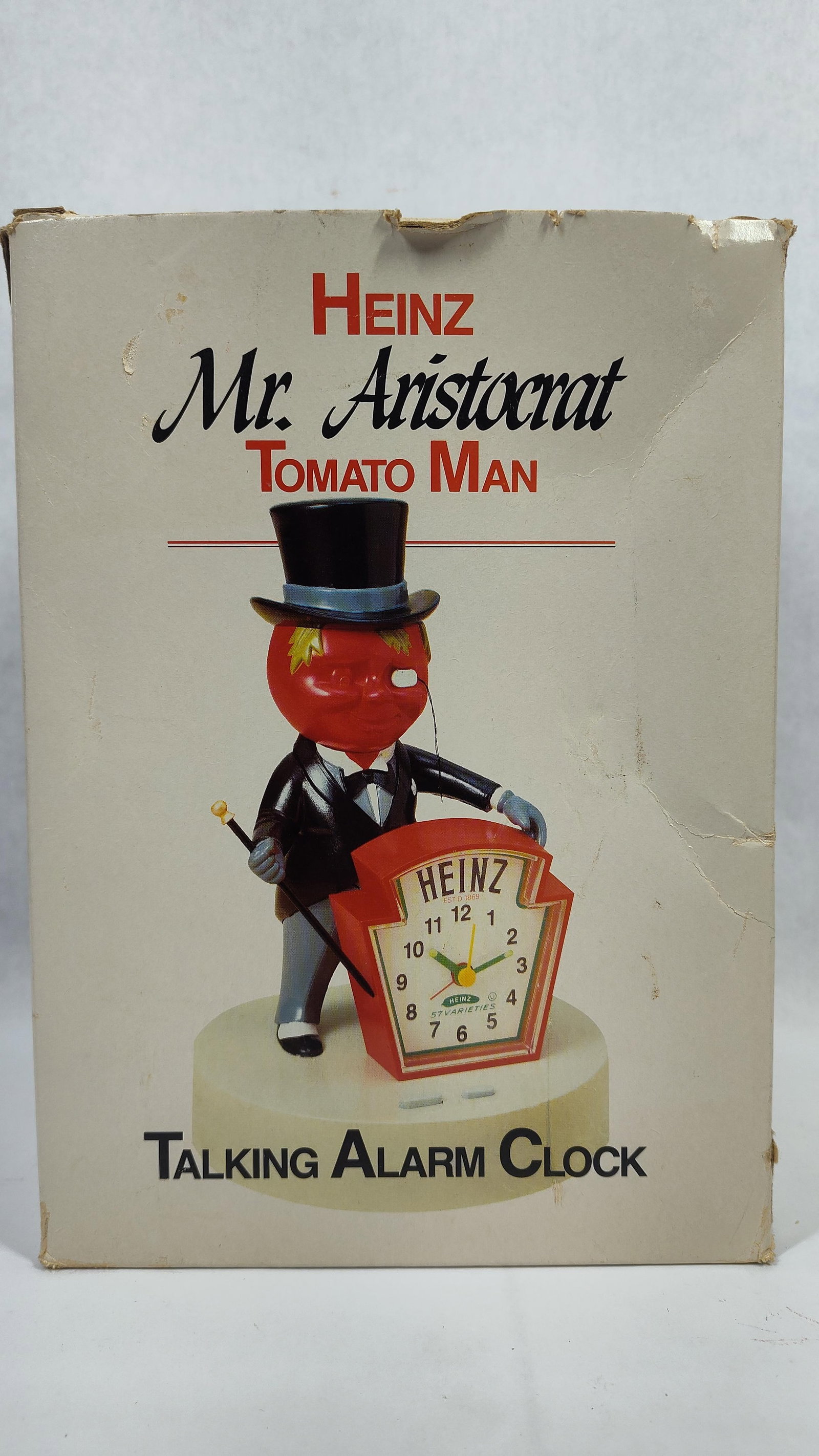 Heinz Mr. Aristocrat Tomato Man Talking Alarm Clock in Original Box: This is apromotional figural talking alarm clock featuring the mascot Mr. Aristocrat Tomato Man, produced for the Heinz company. The character is depicted with a red tomato head and a monocle, wearing