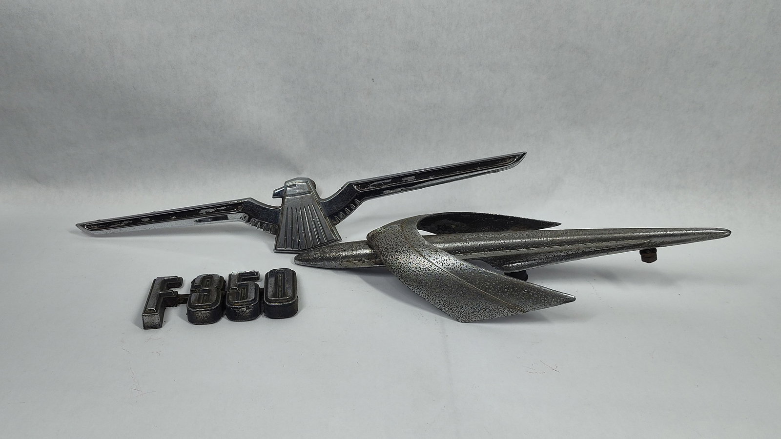 A Trio ofAmerican Automotive Emblems and Hood Mascot including 1955 Chevrolet and Ford F-Series: This lot comprises three originalautomotive exterior trim components. The first item is a Ford F-350 vehicle badge featuring block-style lettering characteristic of F-Series trucks from the late 1950s
