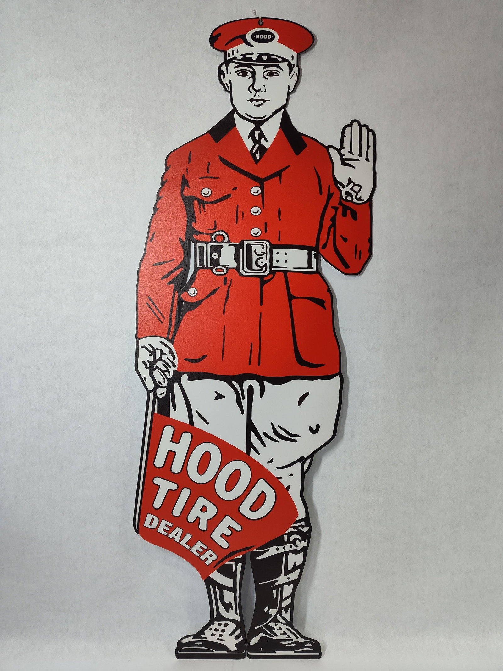 Hood Tire Dealer Die-Cut Metal Advertising Sign: A single-sided, die-cut metal advertising sign for Hood Tires. The sign features the iconic Hood Tire Service Man, a stylized figure of a traffic officer or Mountie dressed in a red uniform tunic with