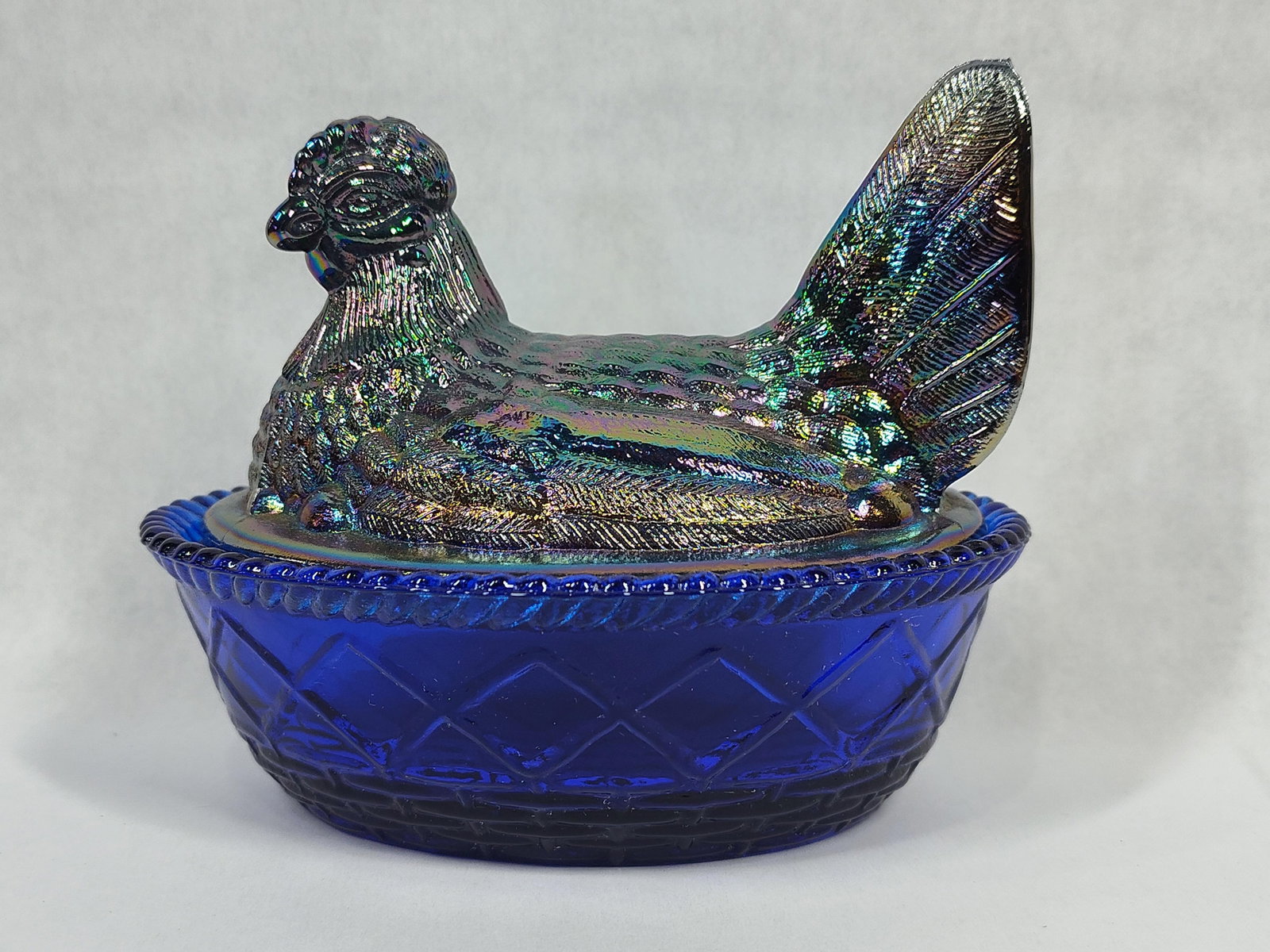 Westmoreland Cobalt Blue Carnival Glass Hen on Nest Covered Dish: A two-piece pressed glass covered dish in the form of a hen on a nest, manufactured by the Westmoreland Glass Company. The lid is sculpted as a nesting hen with detailed feathering and finished with a