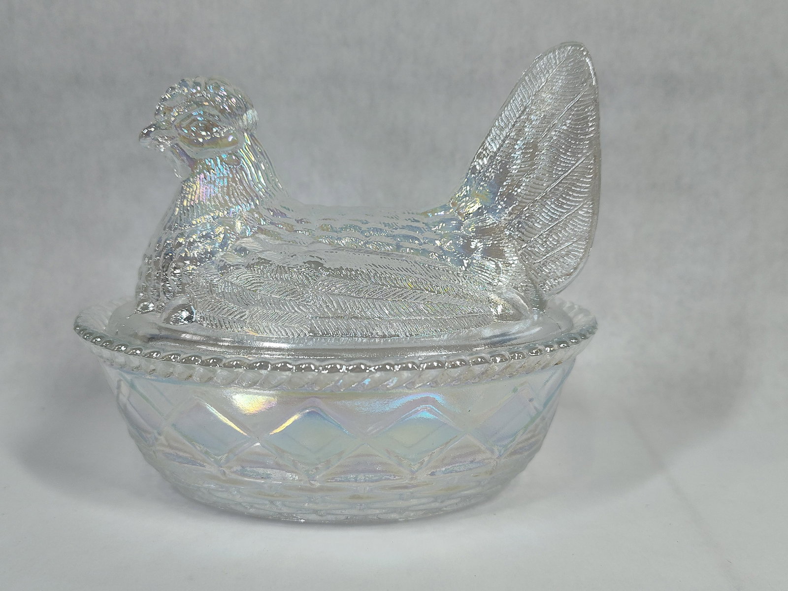L.E. Smith Iridescent Carnival Glass Hen on a Nest Covered Dish: A pressed glass covered dish in the form of a nesting hen, manufactured by the L.E. Smith Glass Company. The item is crafted from clear glass with a pearlescent iridescent finish throughout. The lid