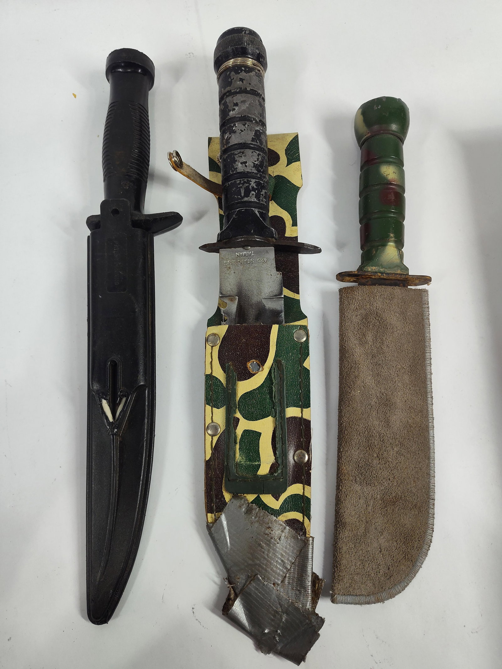 A Trio of Taiwan Stainless Steel Survival Knives: three fixed-blade Rambo-style survival knives produced in Taiwan. This group includes a large survival knife with a 420 stainless steel blade featuring a sawback spine and a black textured hollow