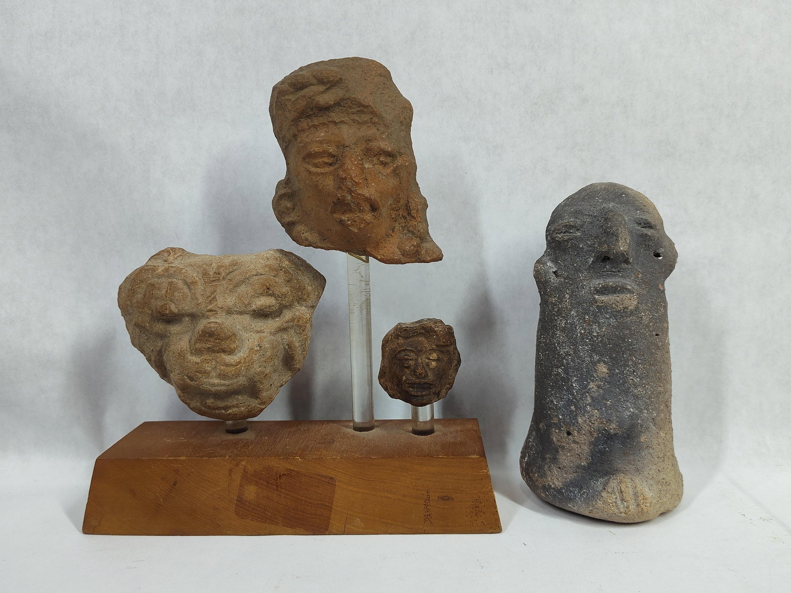 A Group of South American Pre-Columbian Style Ceramic and Stone Artifacts: This group of artifacts consists of several items characteristic of South American Pre-Columbian traditions. The collection features three ceramic terracotta head fragments mounted on a stepped wooden