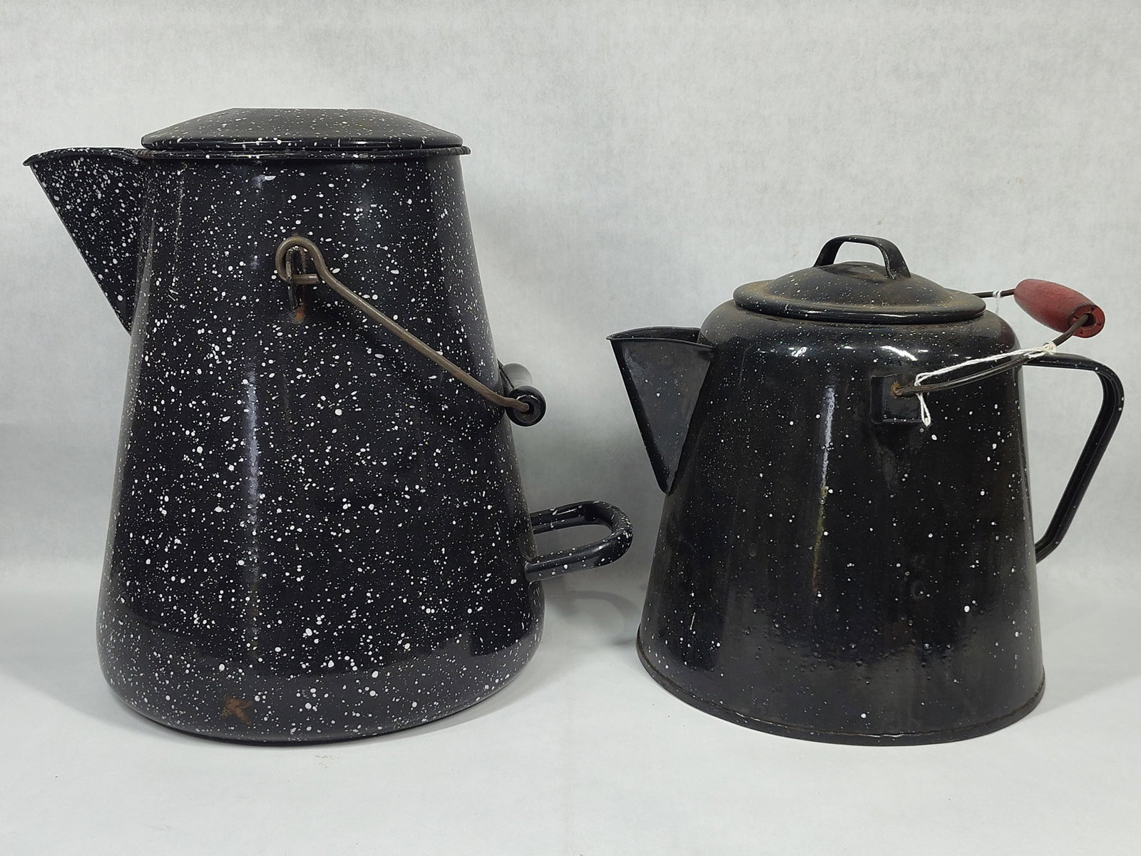 A Pair ofBlack Speckled Enamelware Coffee Pots including a US Navy Vollrath Pot: This lot features two pieces of American graniteware, characterized by a black field with a white speckled finish. One piece is a large, tapered cylindrical coffee boiler manufactured by The Vollrath 