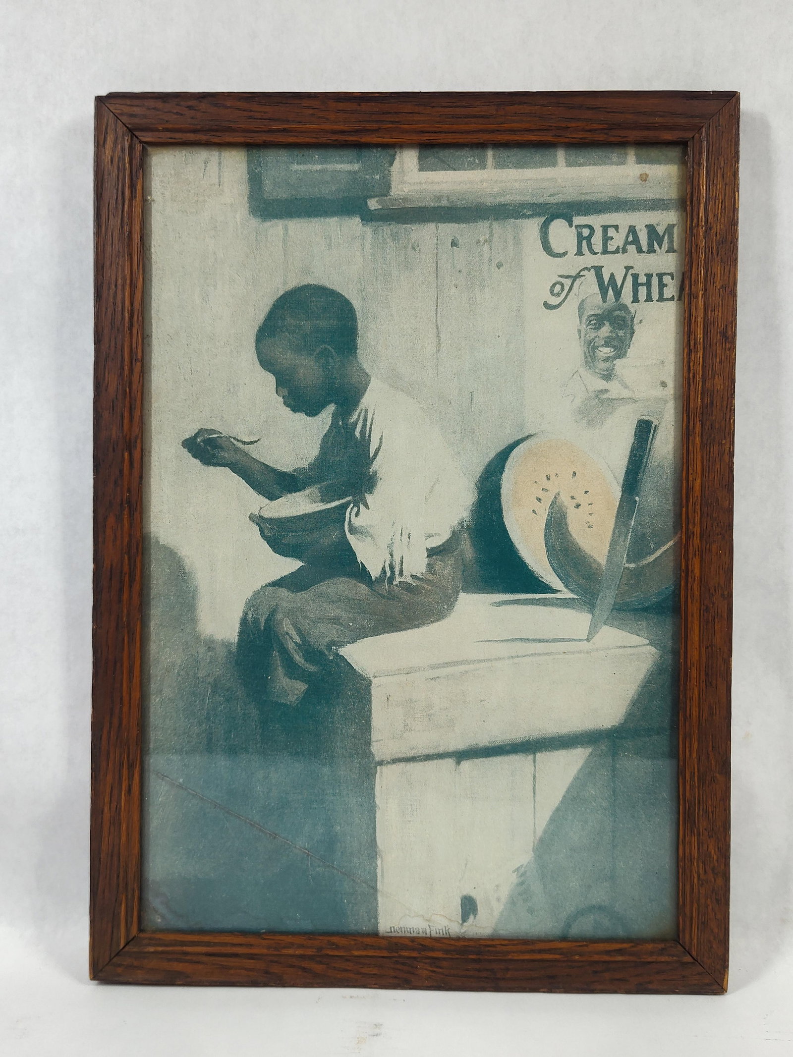 Denman Fink, Cream of Wheat Advertisement, 1909: Thiscommercial color lithograph is an advertisement for Cream of Wheat, featuring an illustration by Denman Fink. The subject depicts a young Black child seated on a wooden crate, eating from a bowl w