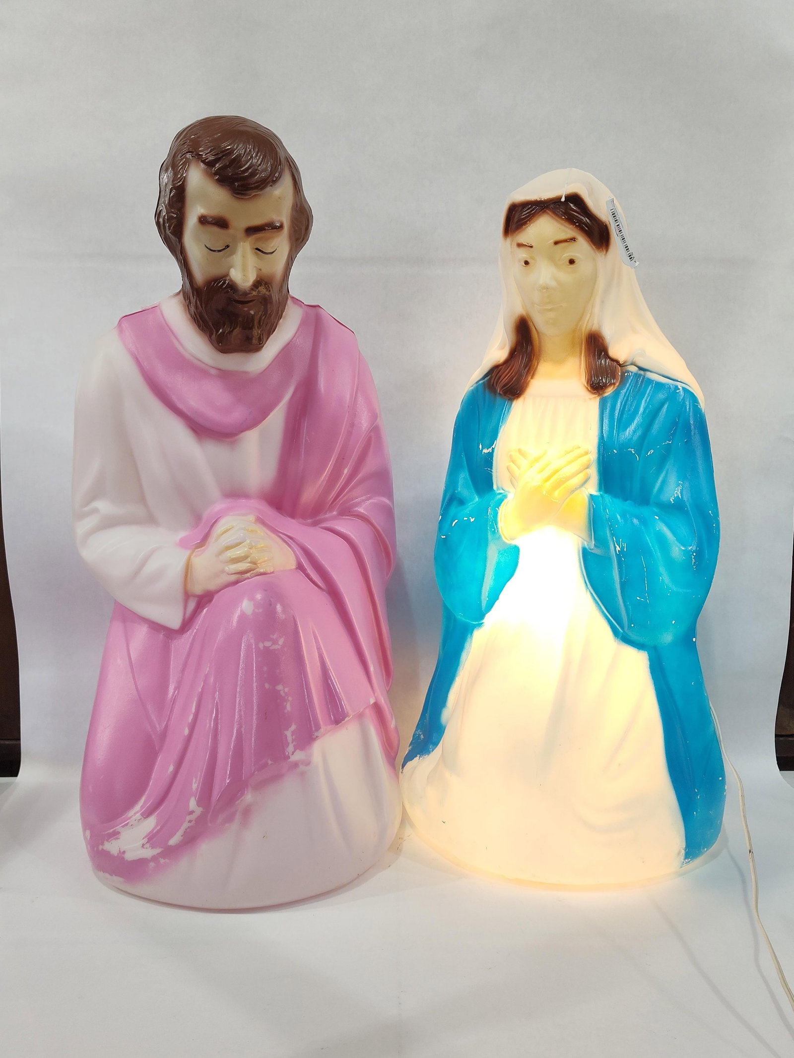A Pair ofEmpire Plastic Corp. Lighted Blow-Mold Nativity Figures, Mary and Joseph: A pair ofblow-mold plastic holiday decorations from a nativity set, manufactured by the Empire Plastic Corp. The set consists of two kneeling figures representing Mary and Joseph. Mary is depicted wea