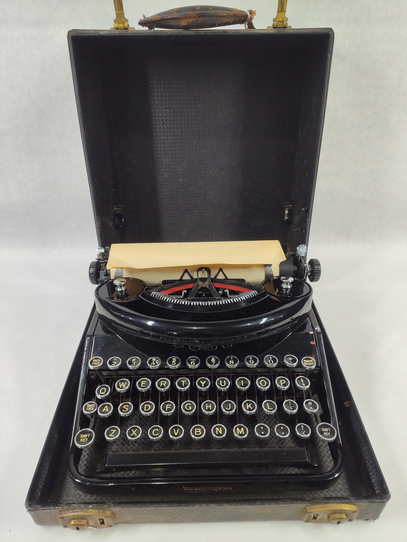 Remington Noiseless Portable Typewriter in Original Carrying Case: ARemington Noiseless Portable typewriter featuring a glossy black enamel finish. The machine is equipped with a four-bank QWERTY keyboard consisting of circular, metal-rimmed keys with white character
