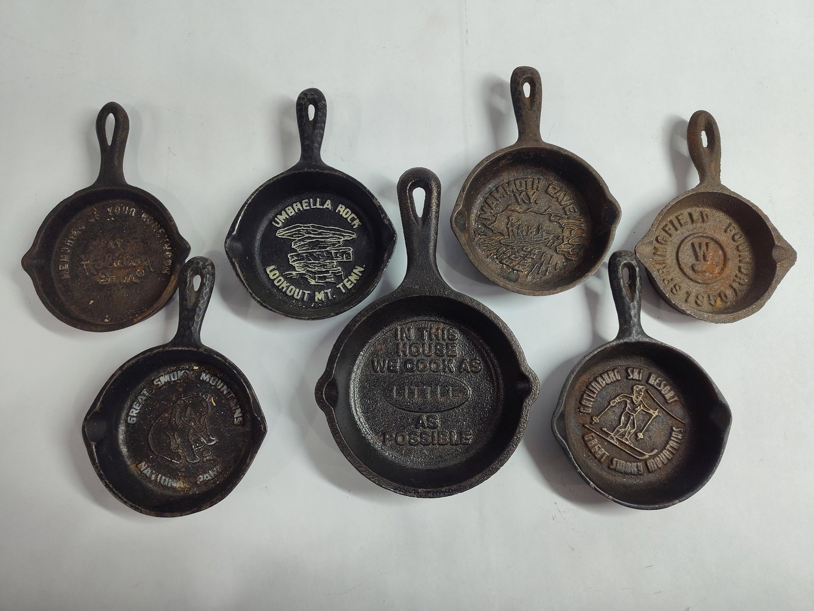 Miniature Cast Iron Advertising and Souvenir Skillets Including Lodge and Wilton: This collection features several miniature cast iron souvenir and advertising skillets, primarily dating from the mid-20th century. A prominent piece is a Lodge Manufacturing Company skillet embossed 