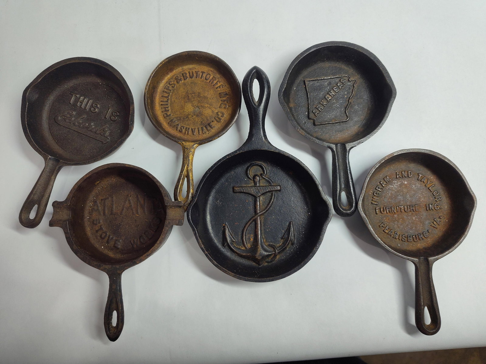SixCast Iron Advertising Skillets and Promotional Items: This lot features sixminiature cast iron advertising skillets and promotional novelty items, typically used as paperweights, ashtrays, or sales giveaways. The group contains an Eckert's promotional sk