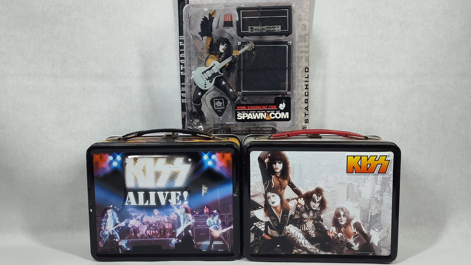 A Trio of KISS Memorabilia Including McFarlane Action Figure and Metal Lunchbox Sets with Thermoses: This collection of music memorabilia consists of three pieces related to the rock band KISS. The first item is a McFarlane Toys action figure of Paul Stanley as The Starchild from the KISS Alive serie