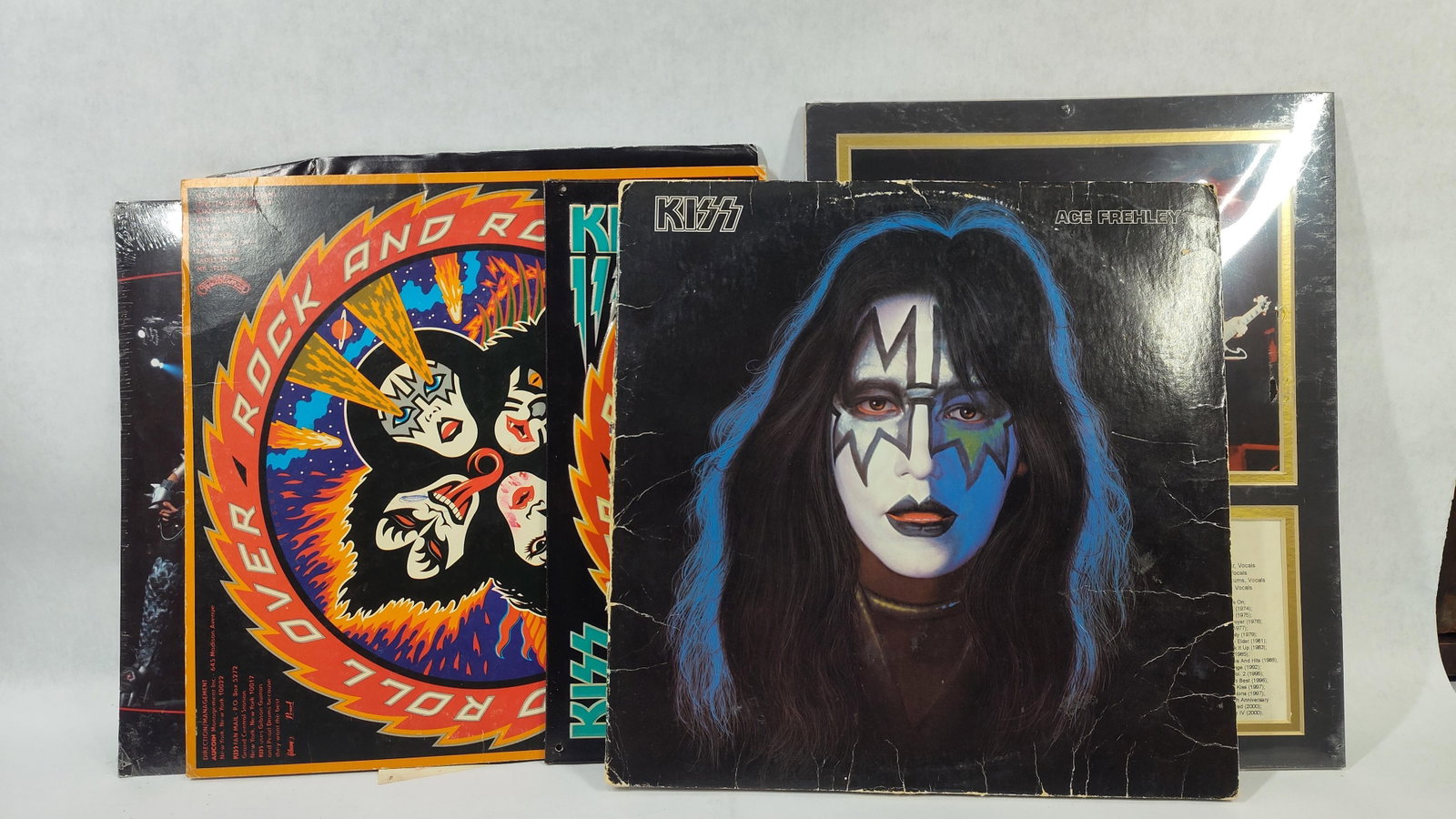 KISS Band Memorabilia Including Vinyl Records, Calendar, and Metal Signs: This lot features memorabilia related to the American rock band KISS. The collection includes two 12-inch vinyl LP records. The first is the 1976 studio album Rock and Roll Over, released by Casablanc