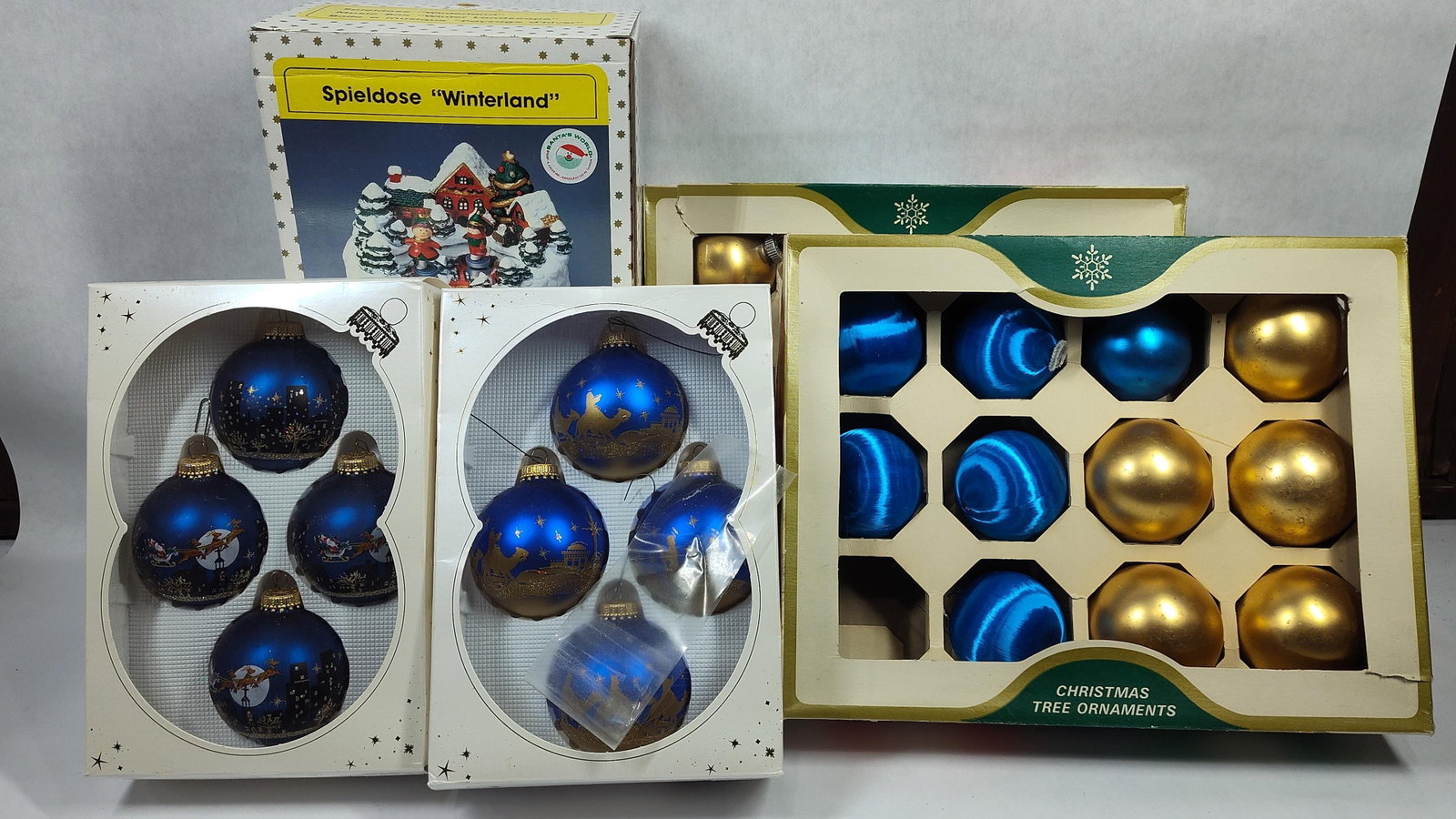 Christmas Decorations Including a Kurt S. Adler Music Box and Glass Ornaments: This assortment ofholiday decor features a mechanical music box and multiple sets of tree ornaments. The music box is housed in its original packaging labeled Spieldose Winterland under the Santa's Wo