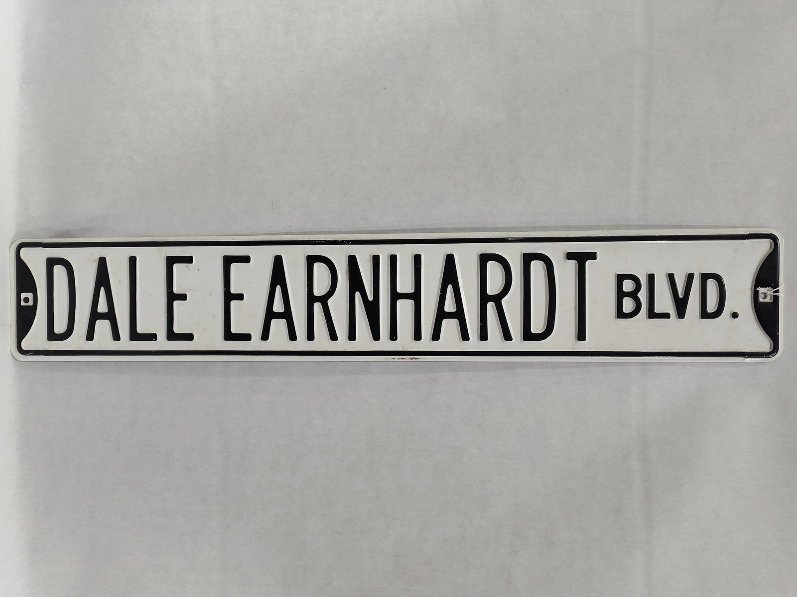 Dale Earnhardt Commemorative Embossed Metal Street Sign: This commemorative embossed metal street sign honors NASCAR driver Dale Earnhardt. The sign features the text DALE EARNHARDT BLVD. in raised, black-painted capital letters. It is constructed from stam