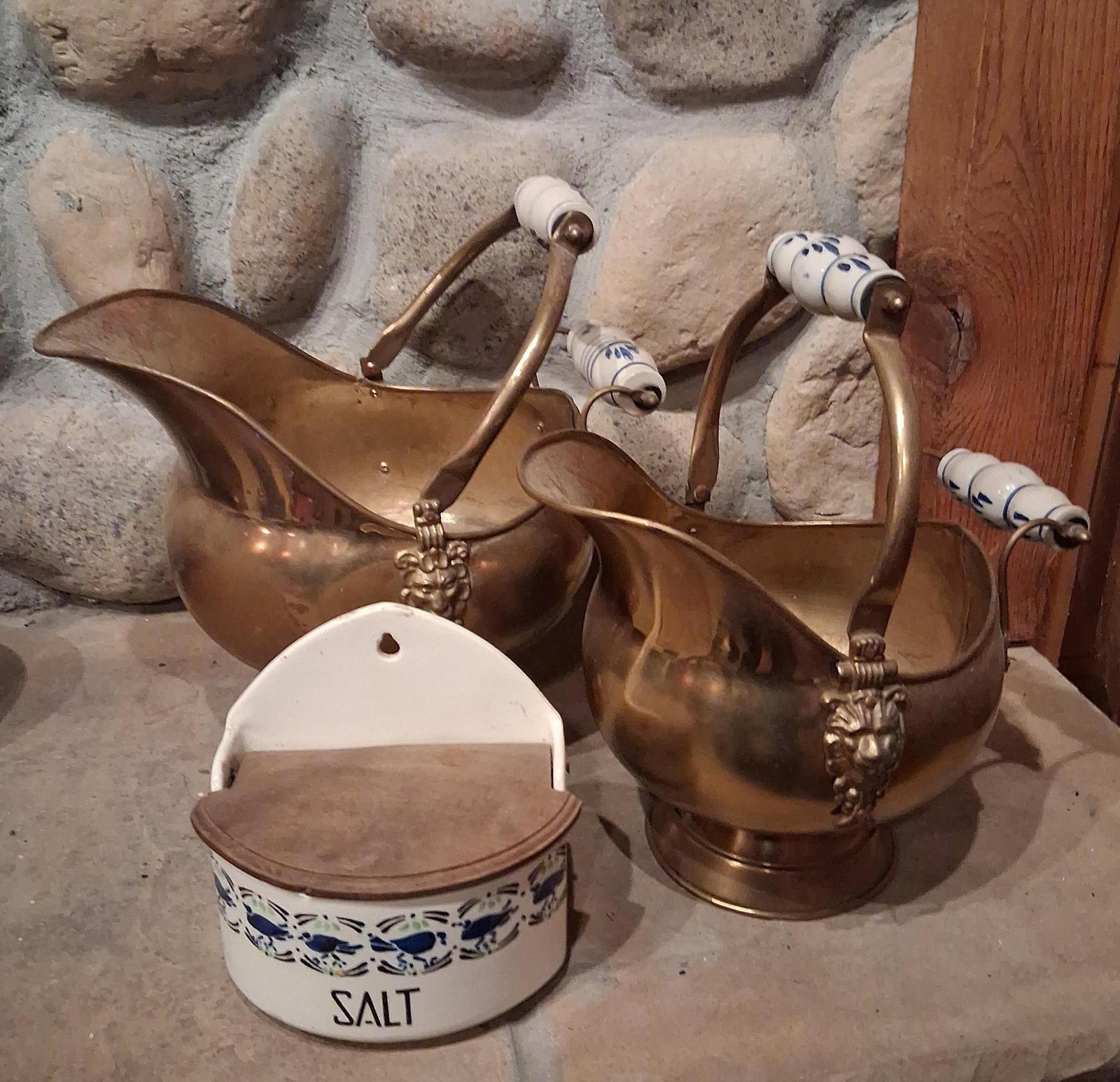 Brass Coal Scuttles w/ Delft & Ceramic Salt Box: This lot consists of a pair of brass fireside coal scuttles and a wall-hanging ceramic salt box. The scuttles are designed in a traditional helmet form, constructed from sheet brass with flared