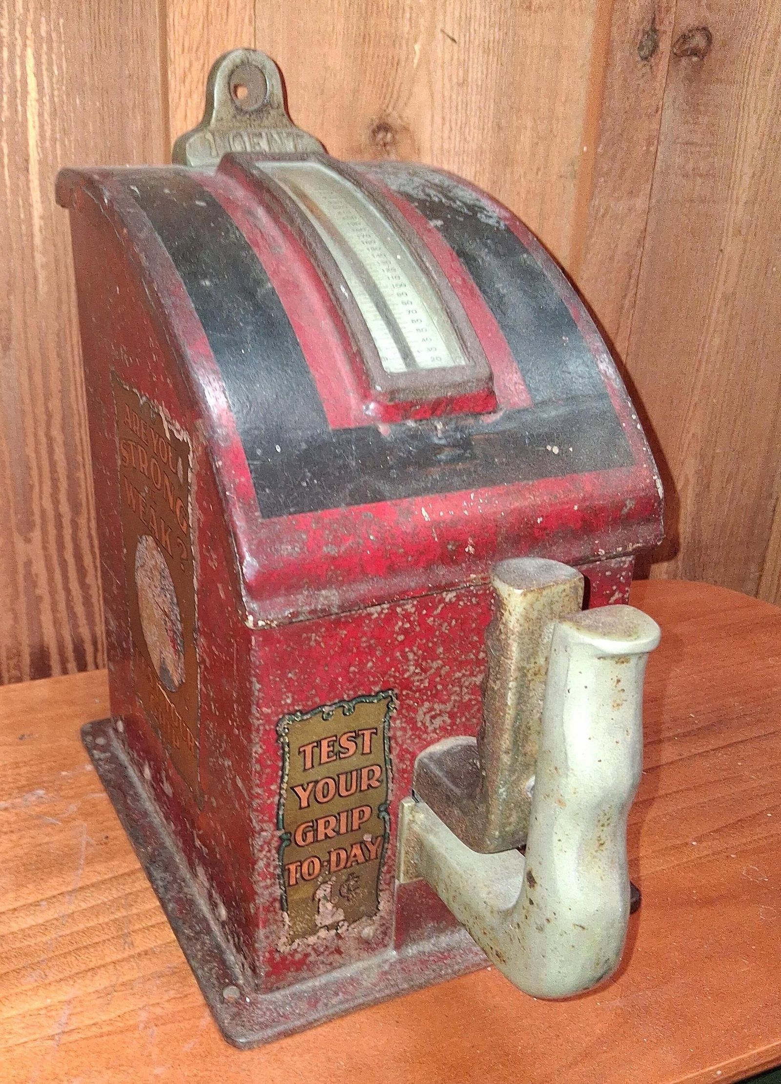 1 Cent Coin Operated Arcade Grip Strength Tester: This coin-operated arcade machine is a mechanical grip strength tester attributed to the Exhibit Supply Company (ESCO). The unit features an A-frame cast iron housing with a red and black painted
