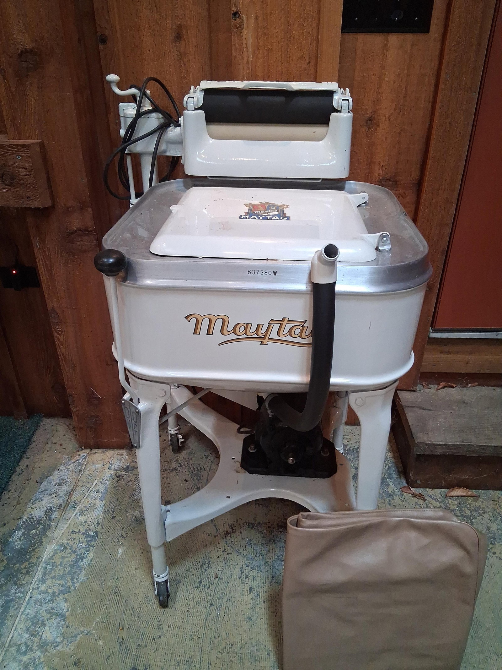Vintage Maytag Electric Wringer Washing Machine: A vintage electric wringer washing machine manufactured by Maytag, featuring a white enameled square-form tub. The unit is supported by a white three-legged metal base equipped with casters for