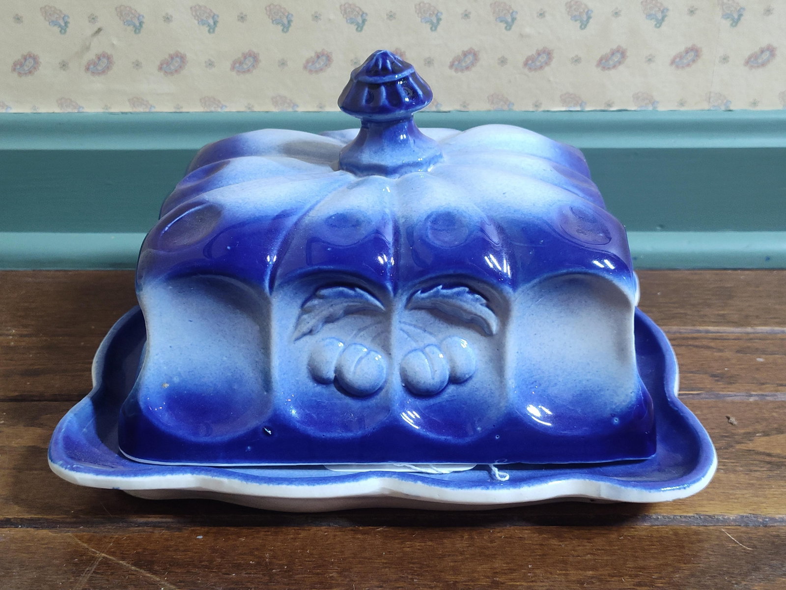 Flow Blue Ironstone Covered Butter Dish w/ Fruit: This is a two-piece ceramic covered butter dish executed in the flow blue style. The set consists of a rectangular, domed lid and a matching scalloped-edge underplate. The lid features fluted corners