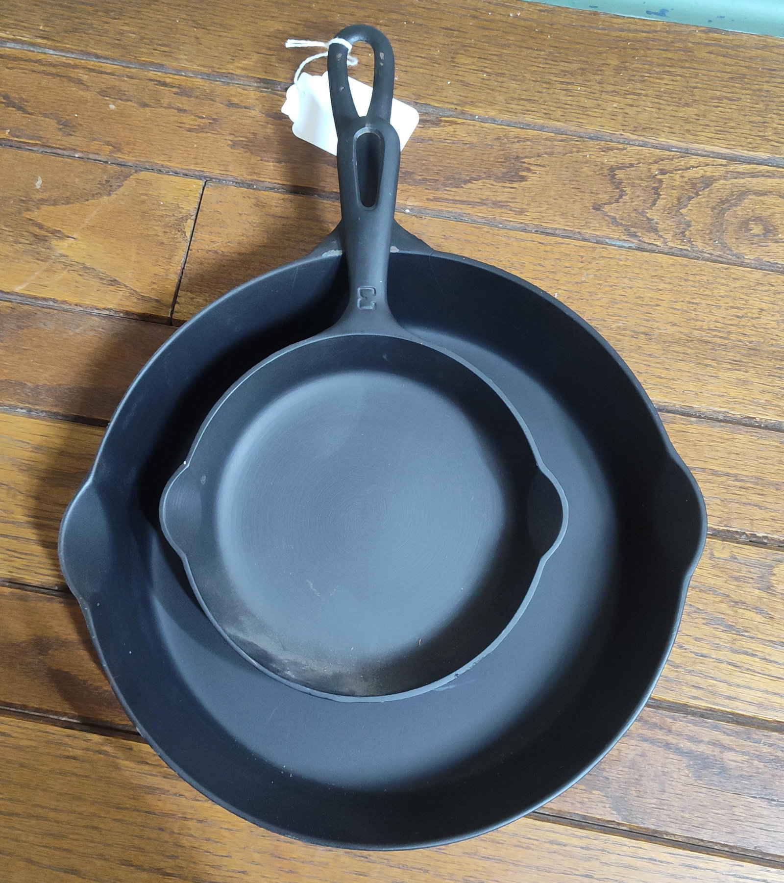 Griswold No. 3 & Erie No. 8 Cast Iron Skillets: This lot features two graduated vintage American cast iron skillets manufactured in Erie, Pennsylvania. The smaller skillet is a No. 3 Griswold model, identifiable by the Griswold small logo on the ba