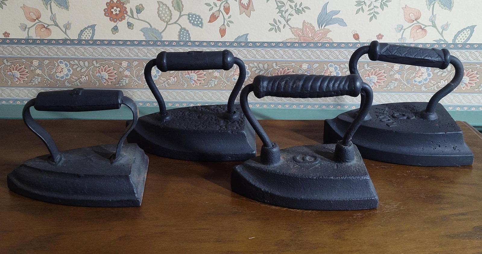 A Group of 4 Antique Cast Iron Sad Irons: A group of 4 antique cast iron sad irons, also known as flat irons, of varying sizes and styles. These items are constructed of solid cast iron and were designed for heating on a stove for domestic