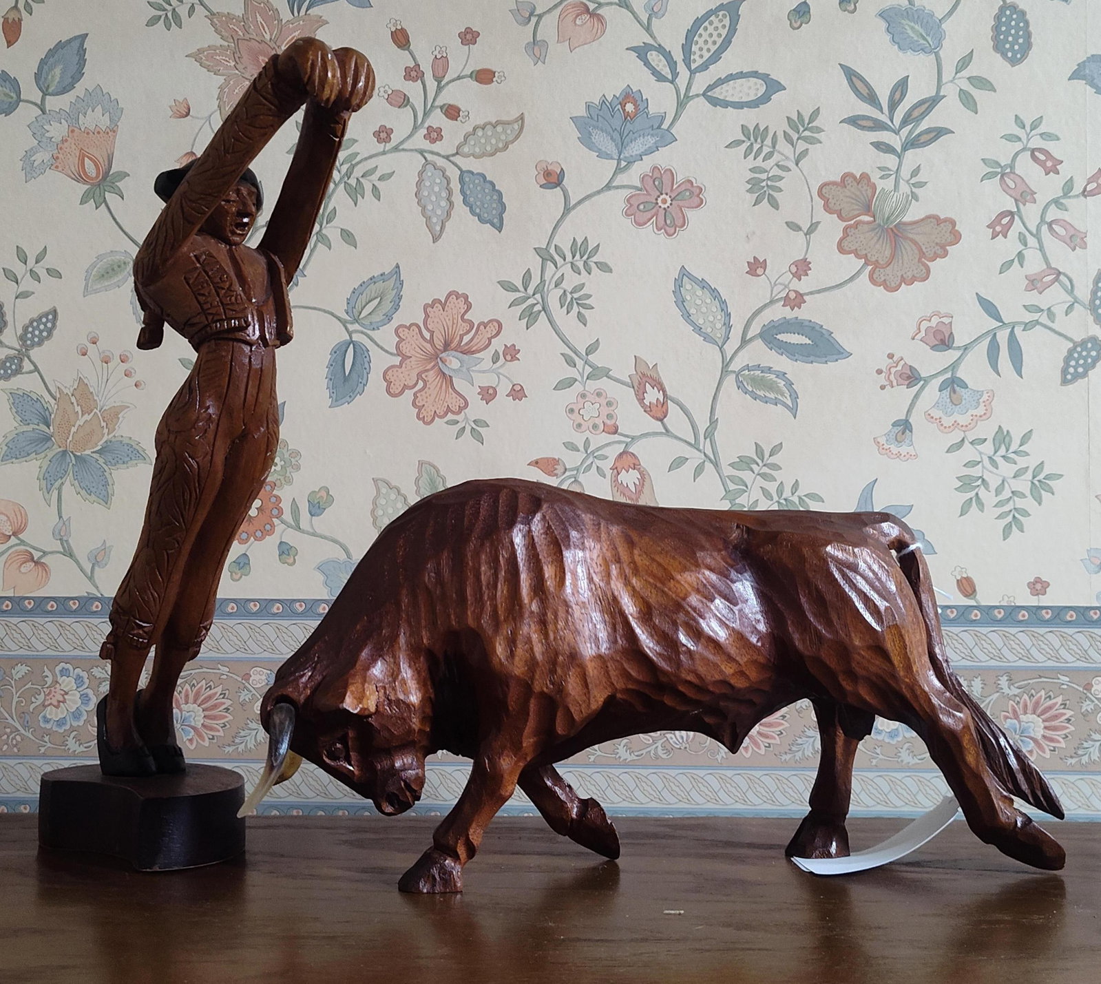 Juan Pinuel Pair Wood Bullfighting Sculptures: This set of two hand-carved wood sculptures by Juan Pinuel portrays a traditional Spanish bullfighting scene. The set includes a matador and a charging bull, both rendered in dark-stained wood with a 