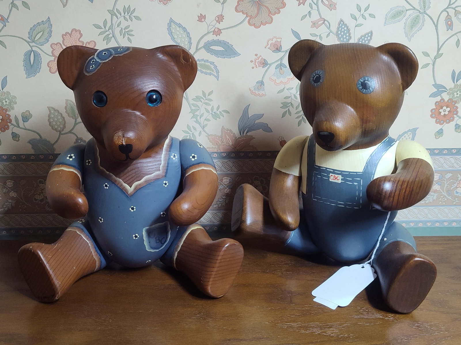 Pair Articulated Painted Carved Wood Teddy Bears: A pair of articulated teddy bear figurines, attributed to the De Vore Country Bear Collection. Each figure is hand-carved from wood with a visible grain, featuring a natural finish on the head, paws,