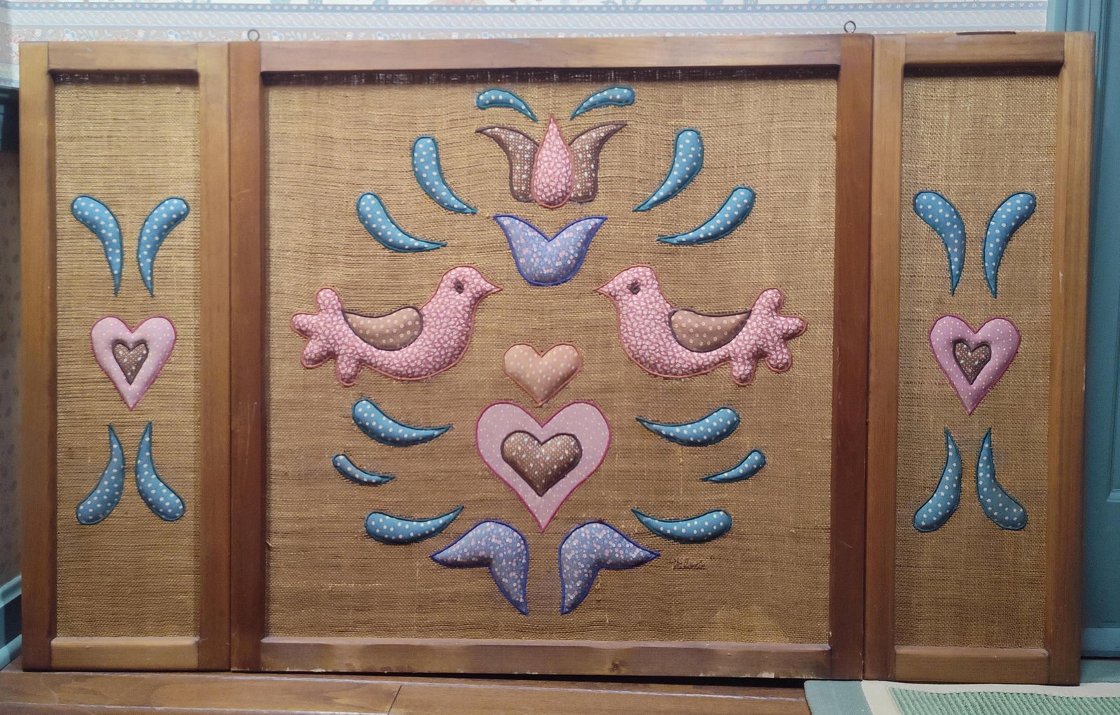 Valerie Trio Folk Art Fabric Applique Hangings: This three-panel set of folk art wall hangings consists of a larger central panel and two narrower flanking panels. Each piece features padded fabric appliqu?s mounted onto a coarse burlap ground,